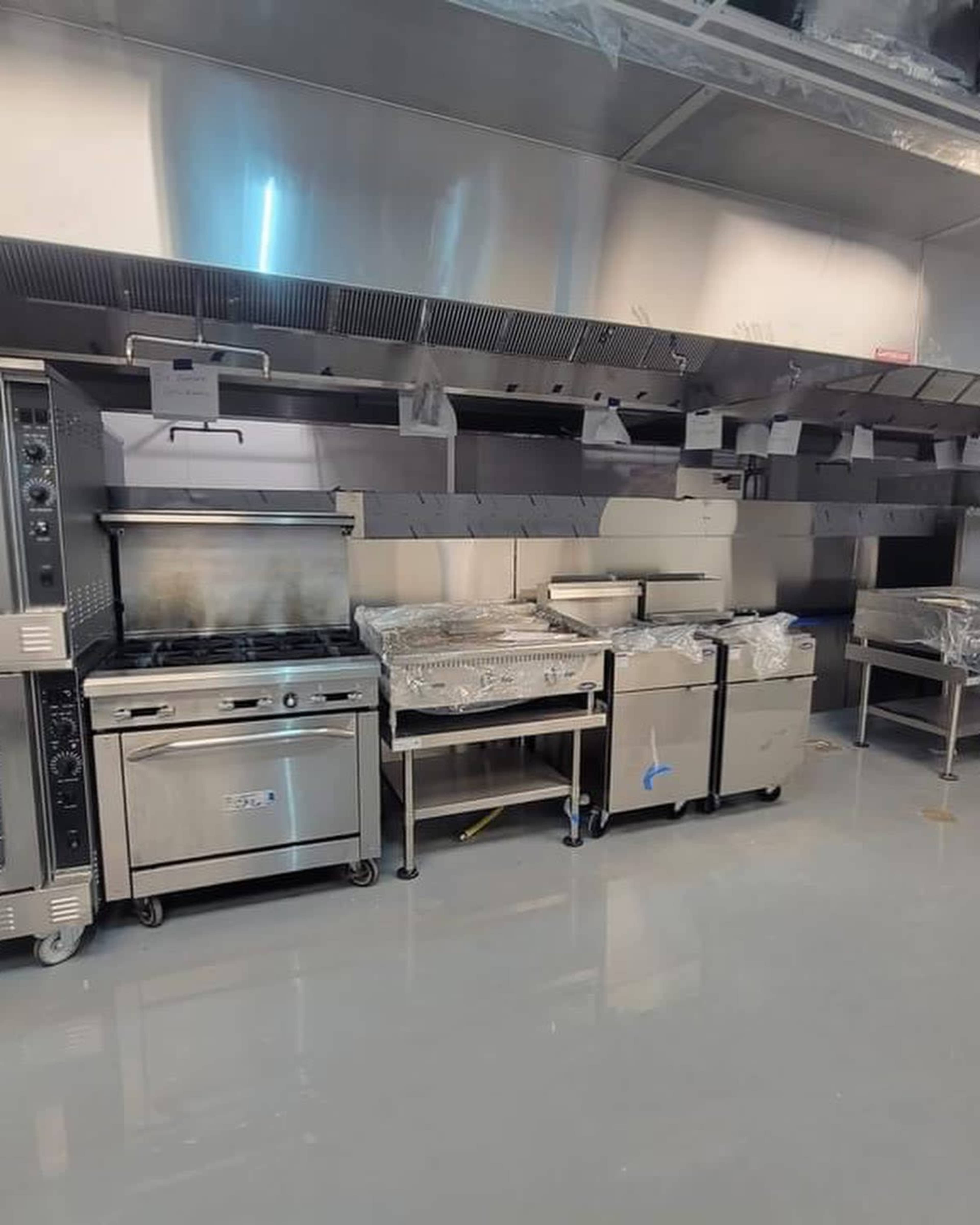 A modern kitchen setup with stainless steel equipment, including an oven, stove, and prep tables, arranged along a clean, clear floor.