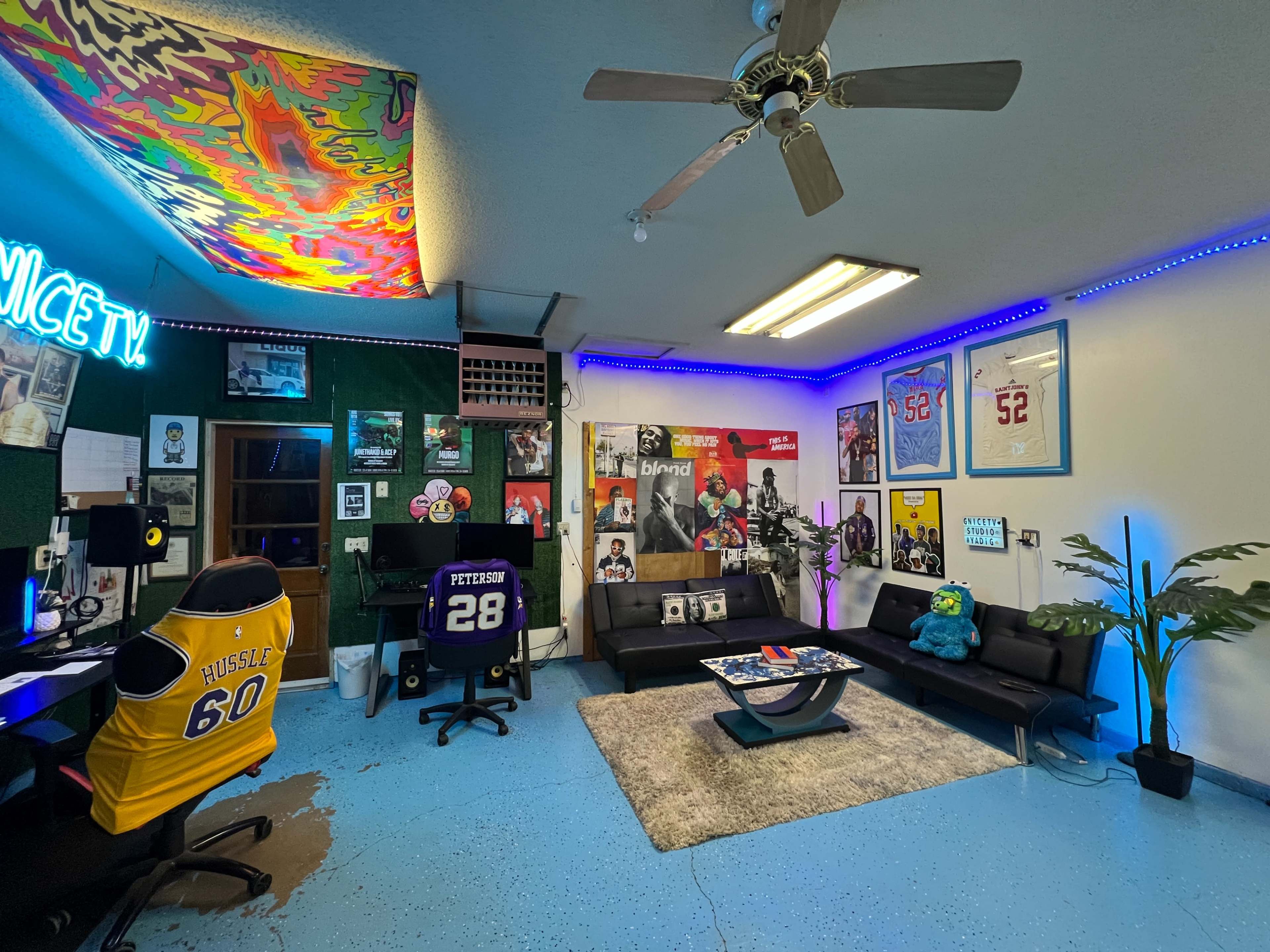 The image shows a colorful sports-themed room with a seating area, wall decorations, and gaming setup, highlighted by neon lights and various framed jerseys.