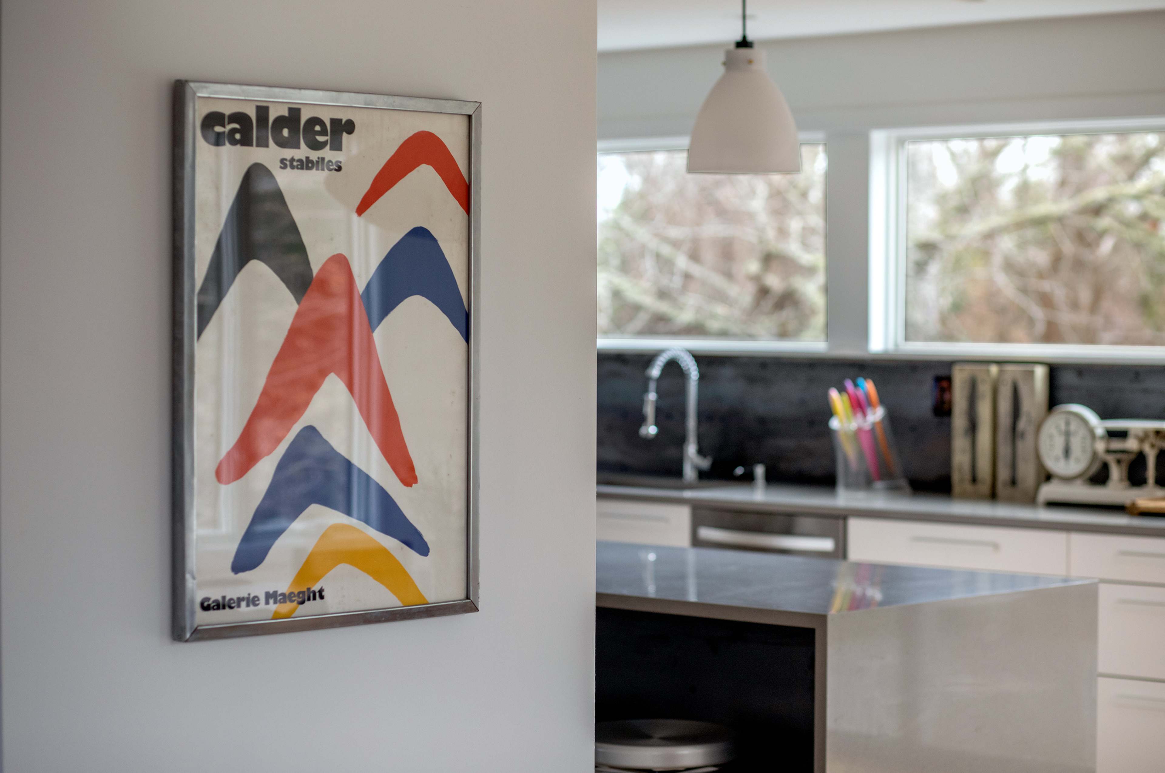 A modern kitchen features a large wall poster of colorful abstract shapes framed on the wall.