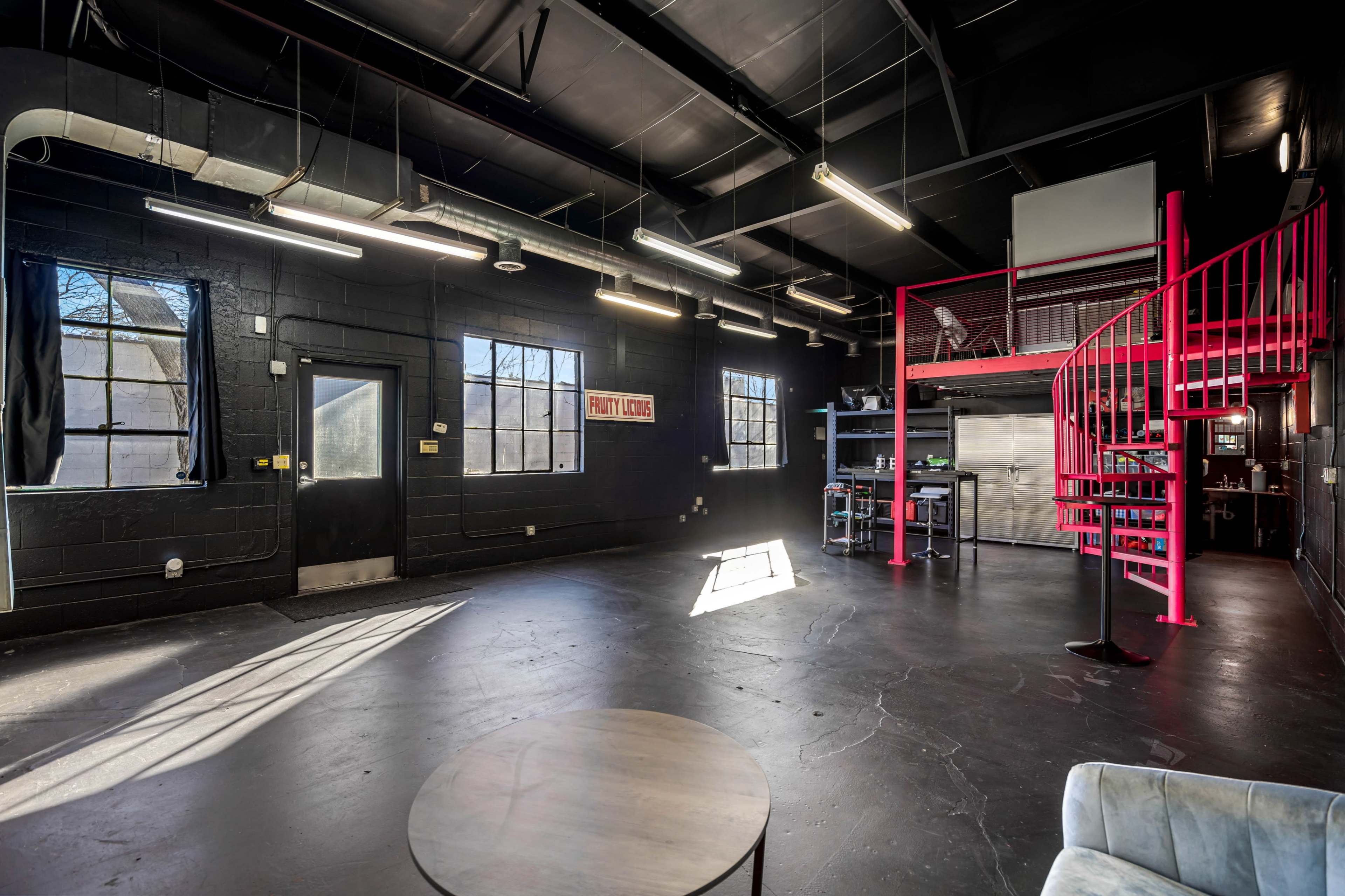 An empty industrial space with black walls, large windows, and a spiral staircase leading to a loft area.