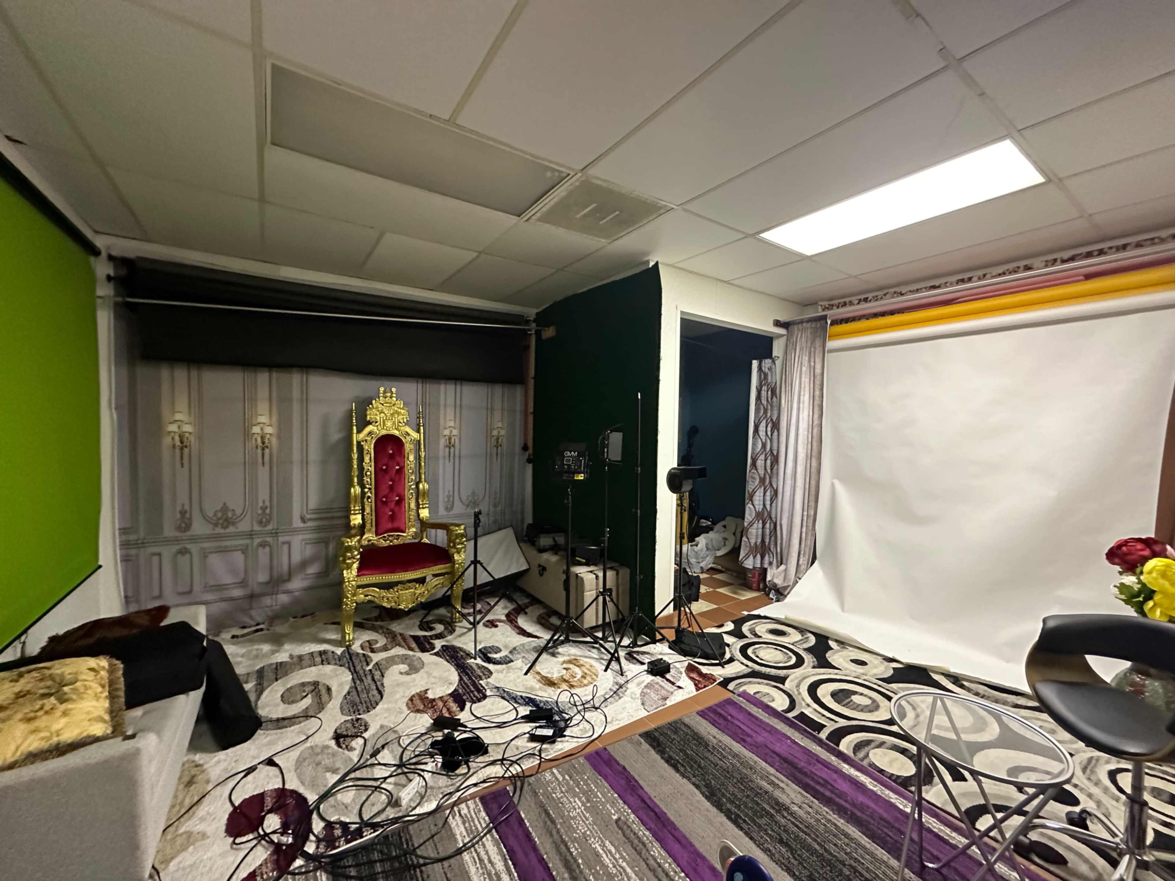 The image shows a photography studio setup with a golden throne, backdrop stands, cables, and various props scattered on the floor.