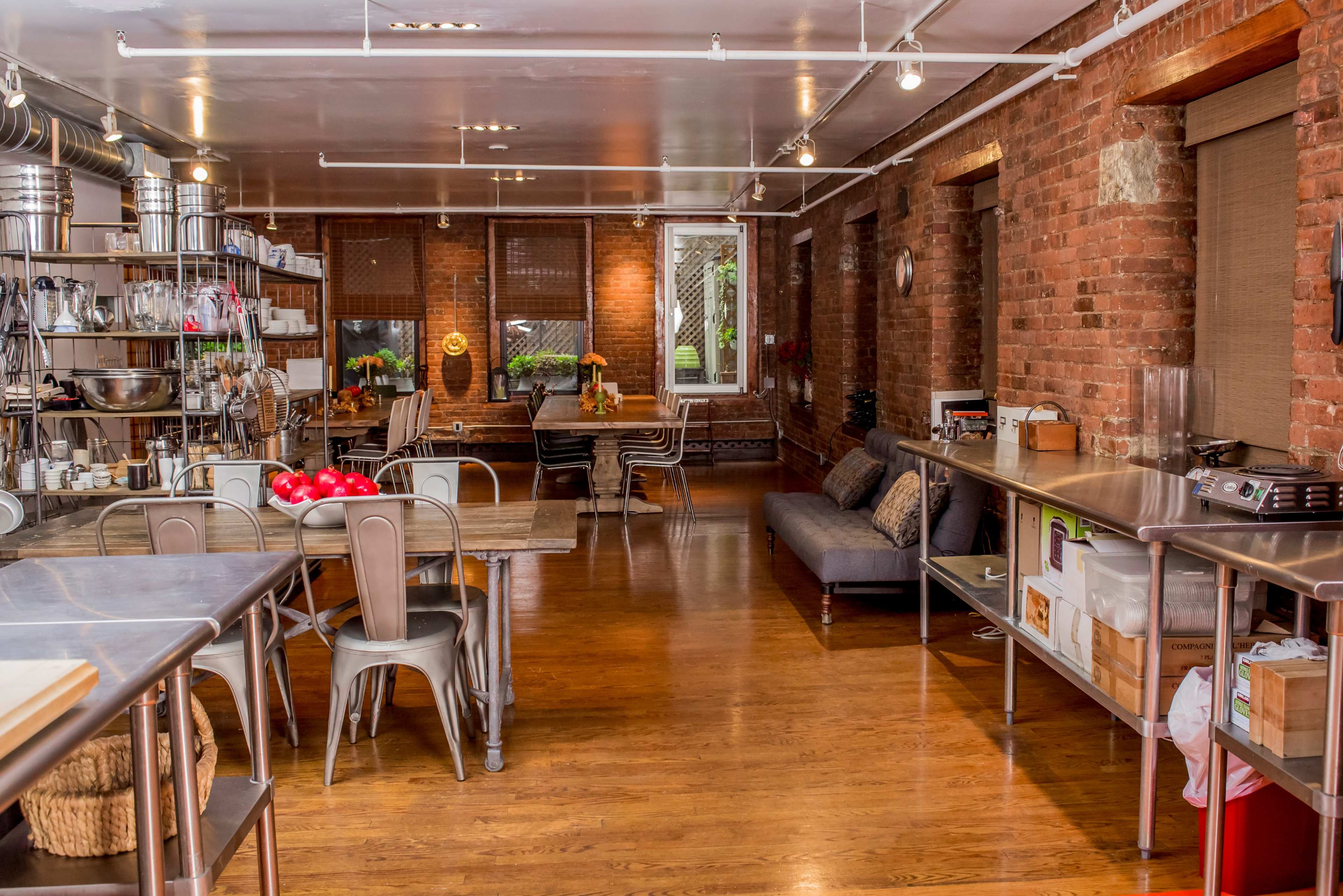 A spacious kitchen area with brick walls, wooden floors, stainless steel counters, and seating arranged around a central space.