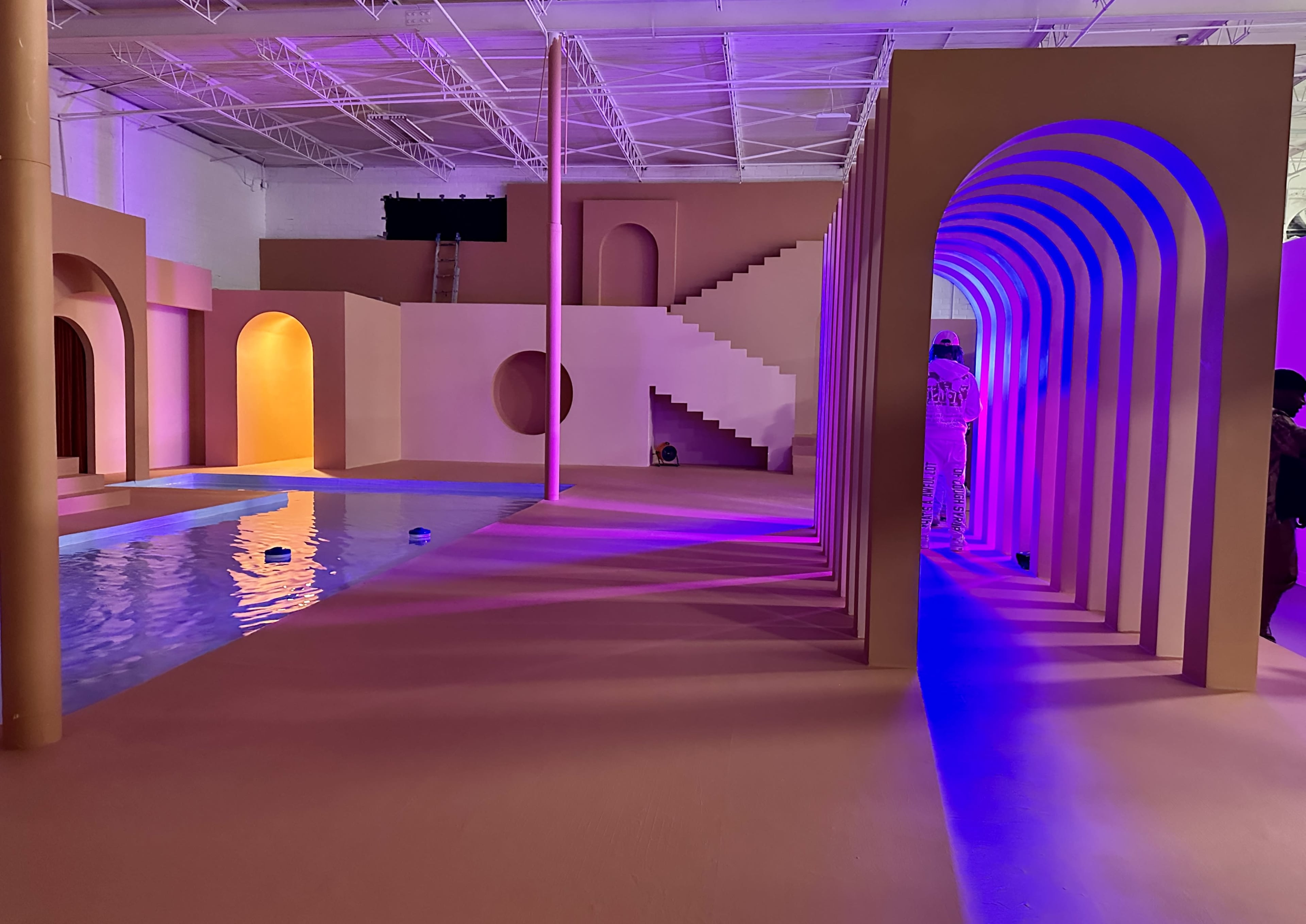An artistic indoor space featuring a pool, geometric structures, and colorful lighting elements.
