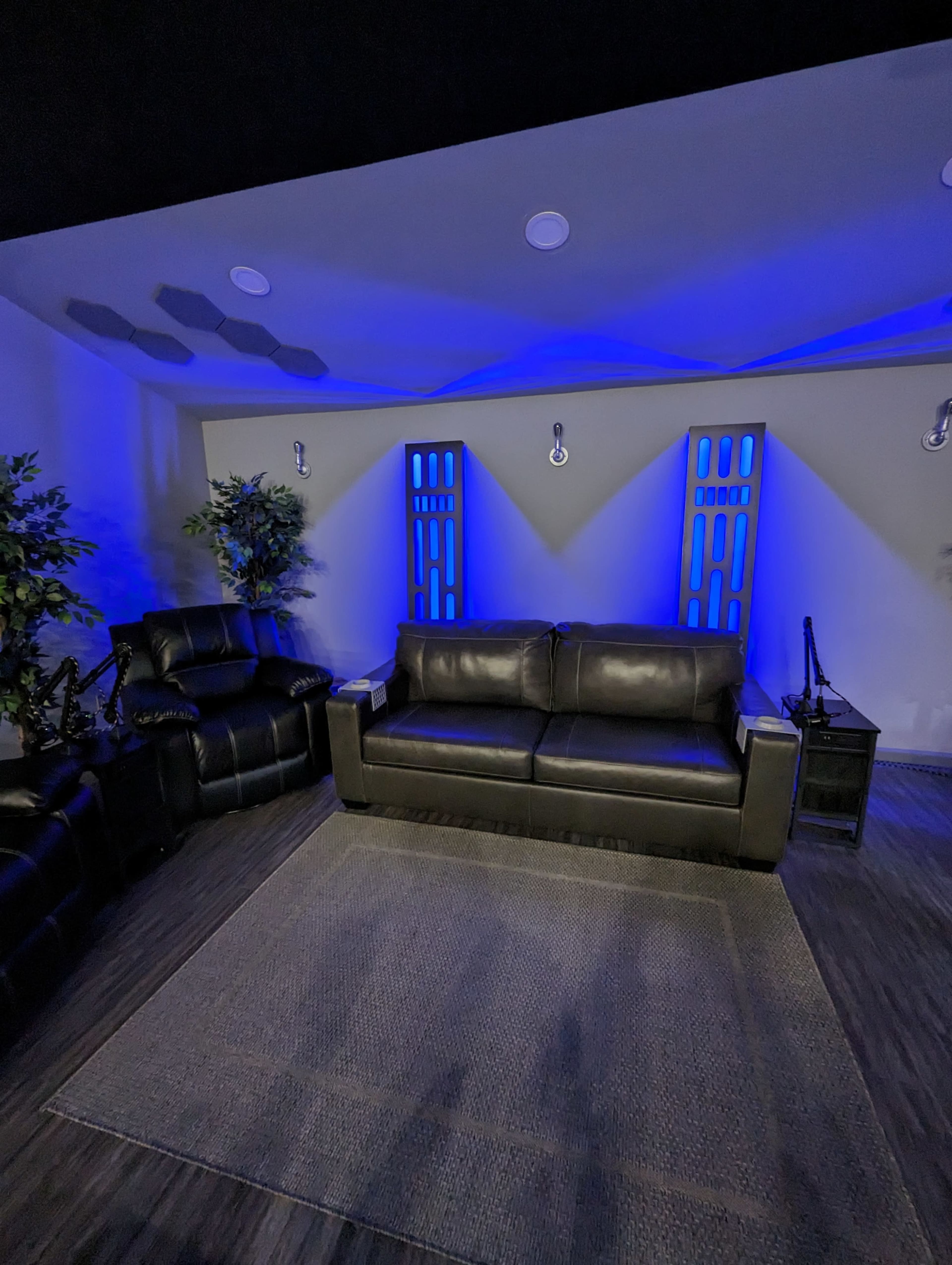 A modern lounge area with a black leather sofa, a recliner, and blue accent lighting against the walls.