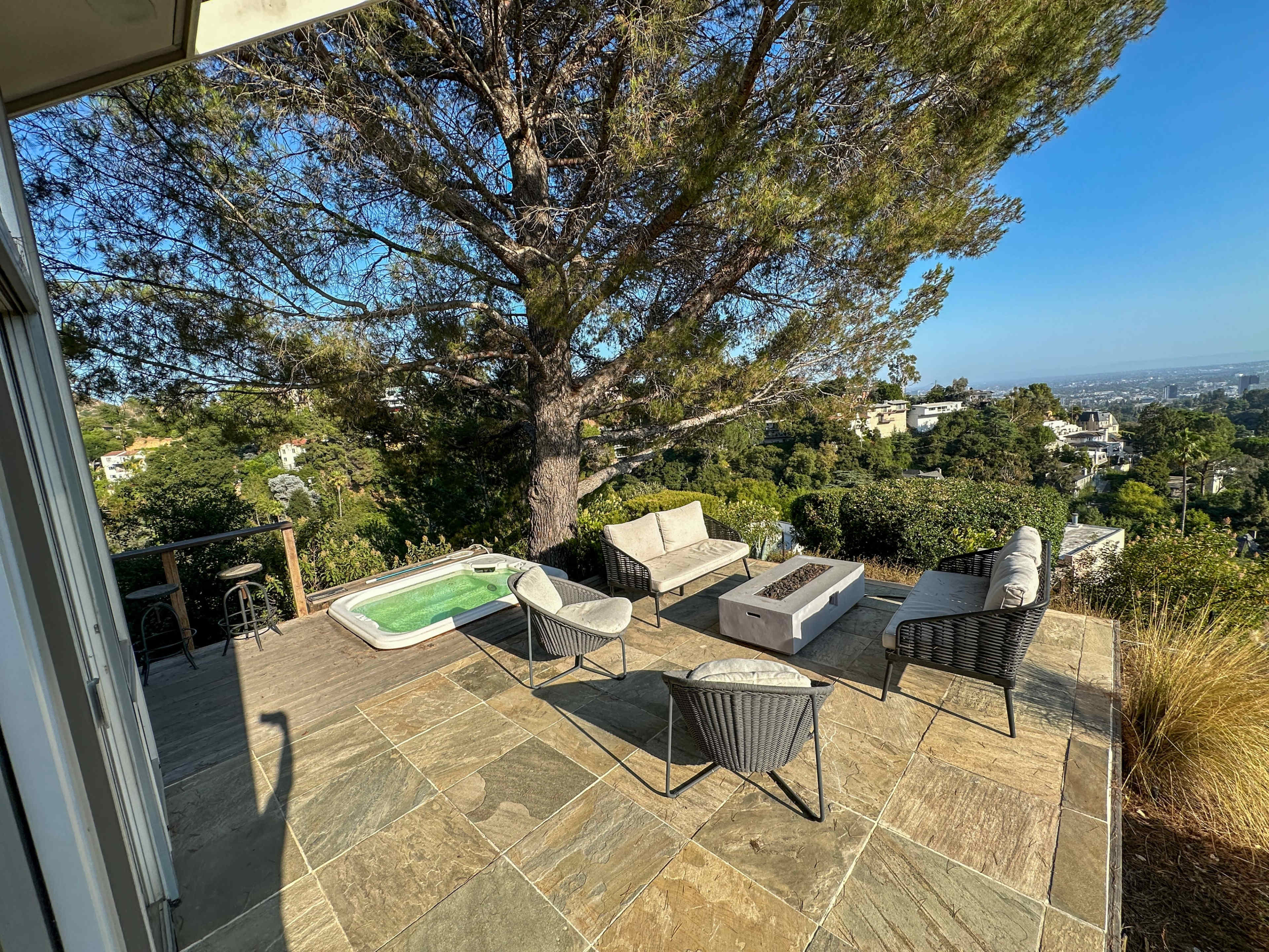 A patio area features outdoor furniture and a small hot tub, overlooking a hilly landscape.