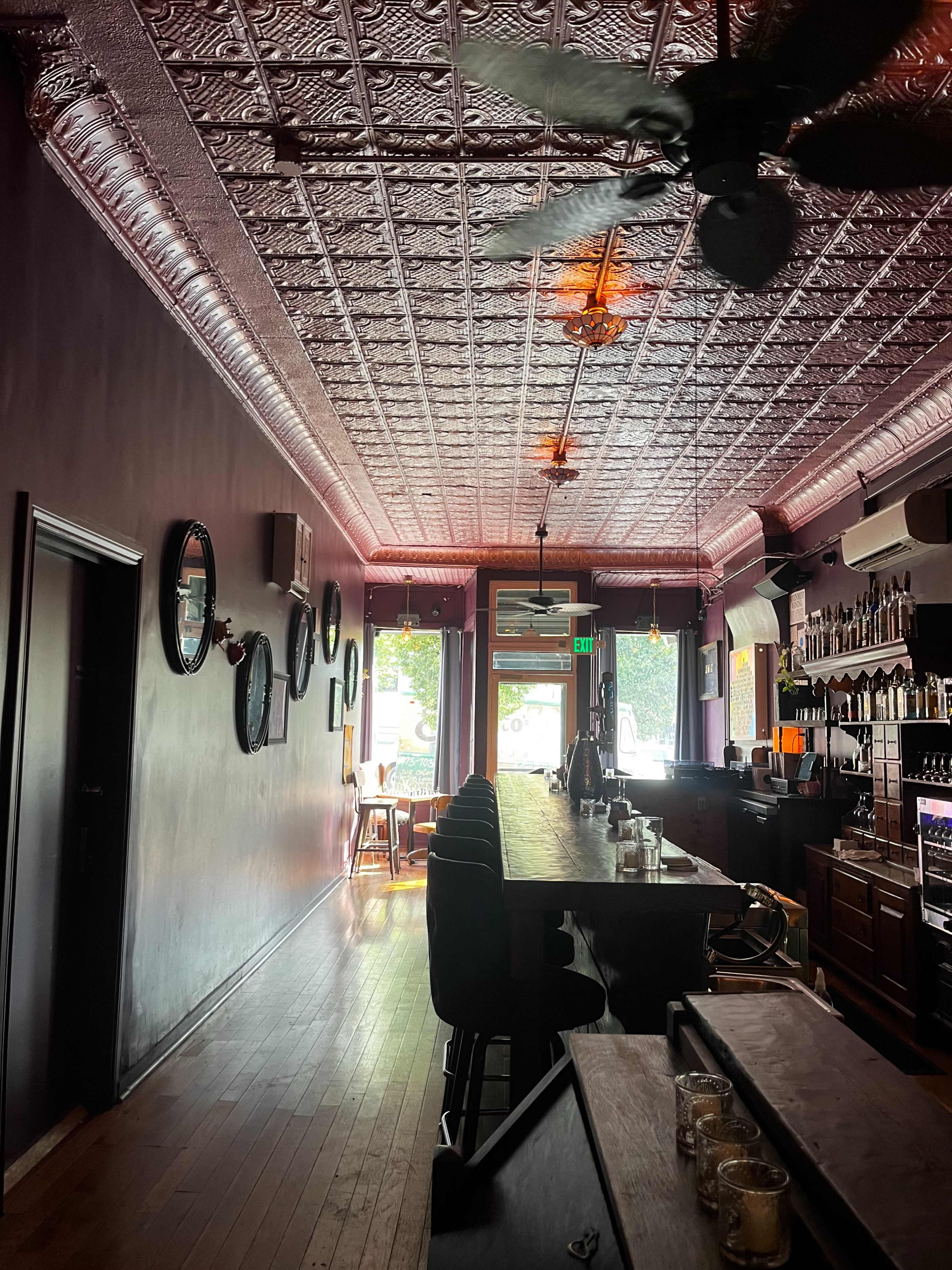 The image shows a long bar area in a dimly lit restaurant with a decorative ceiling and mirrors on the walls.