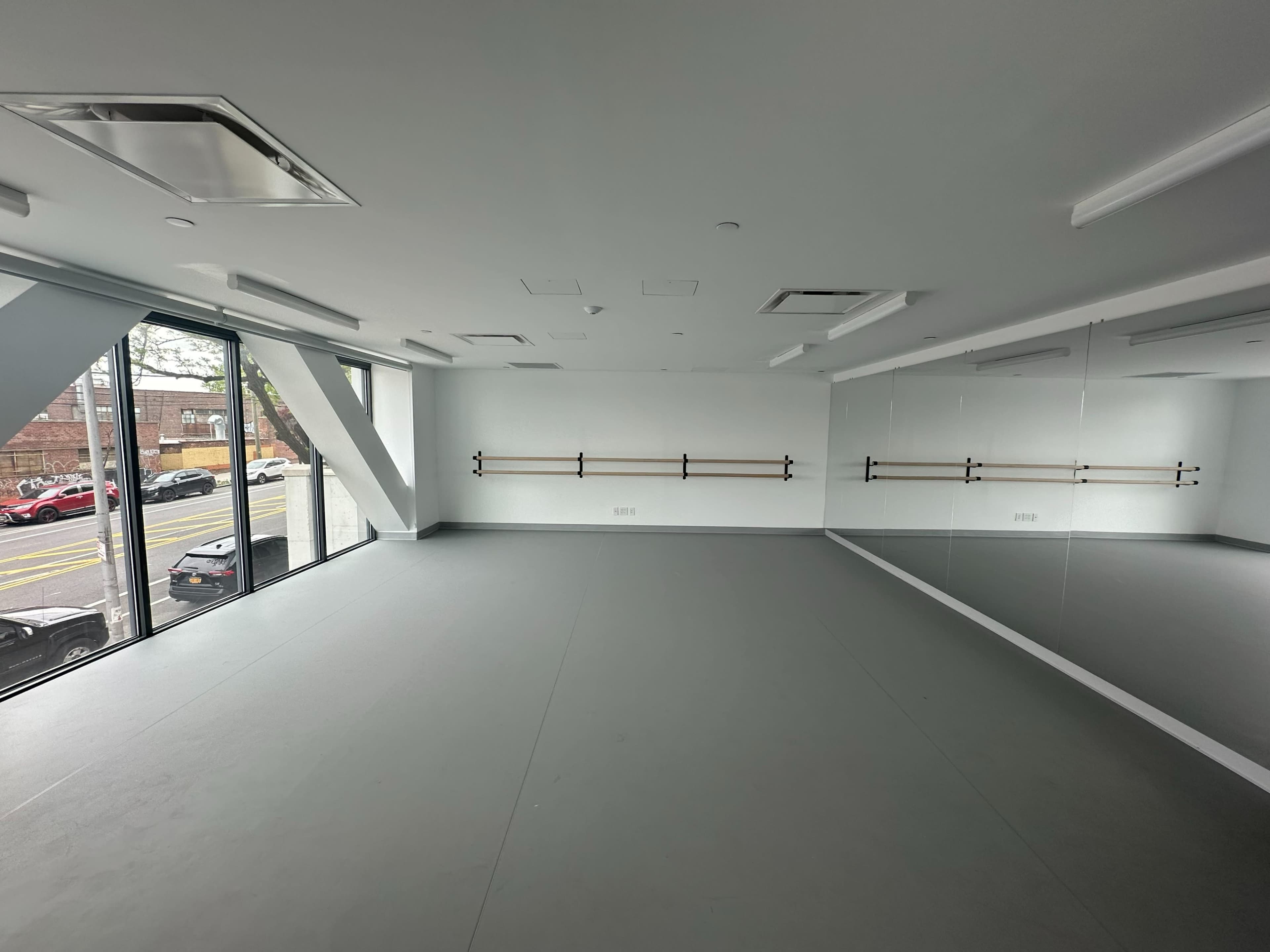 The image shows a spacious, unoccupied studio with large windows and mirrors on one wall.