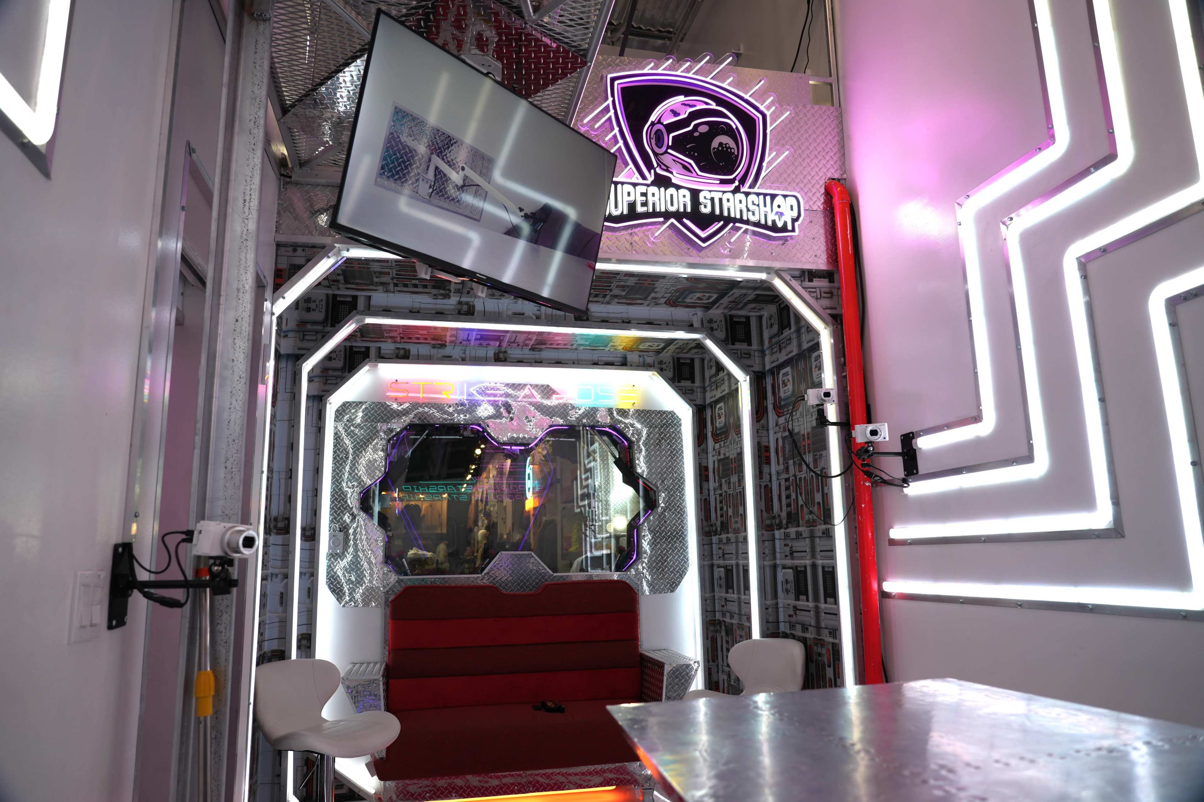 A futuristic-themed room with neon lighting, featuring a red sofa, a large screen, and a sign reading "Superior Starship."
