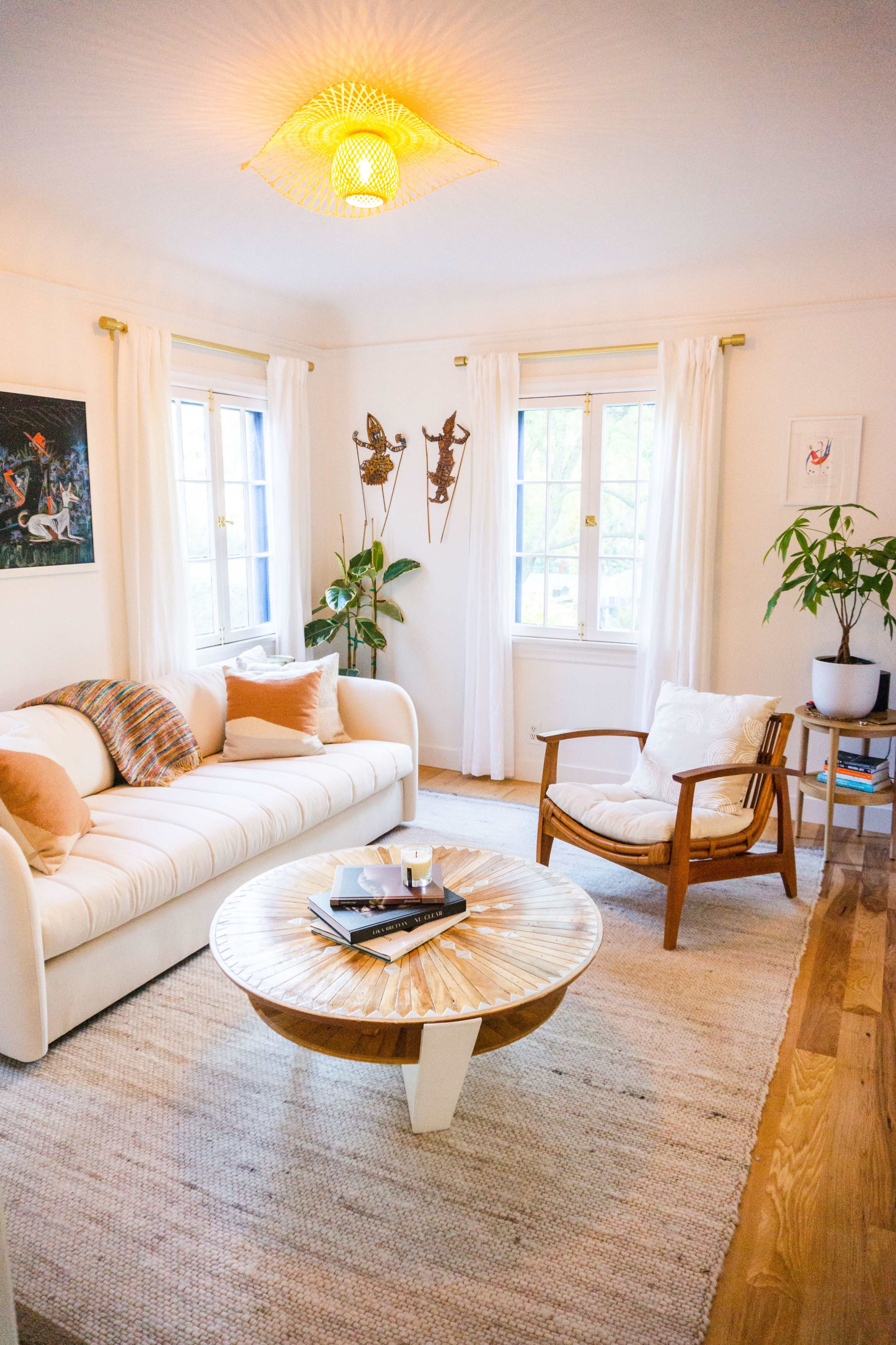 A cozy living room featuring a white sofa, a round coffee table, and large windows with sheer curtains.