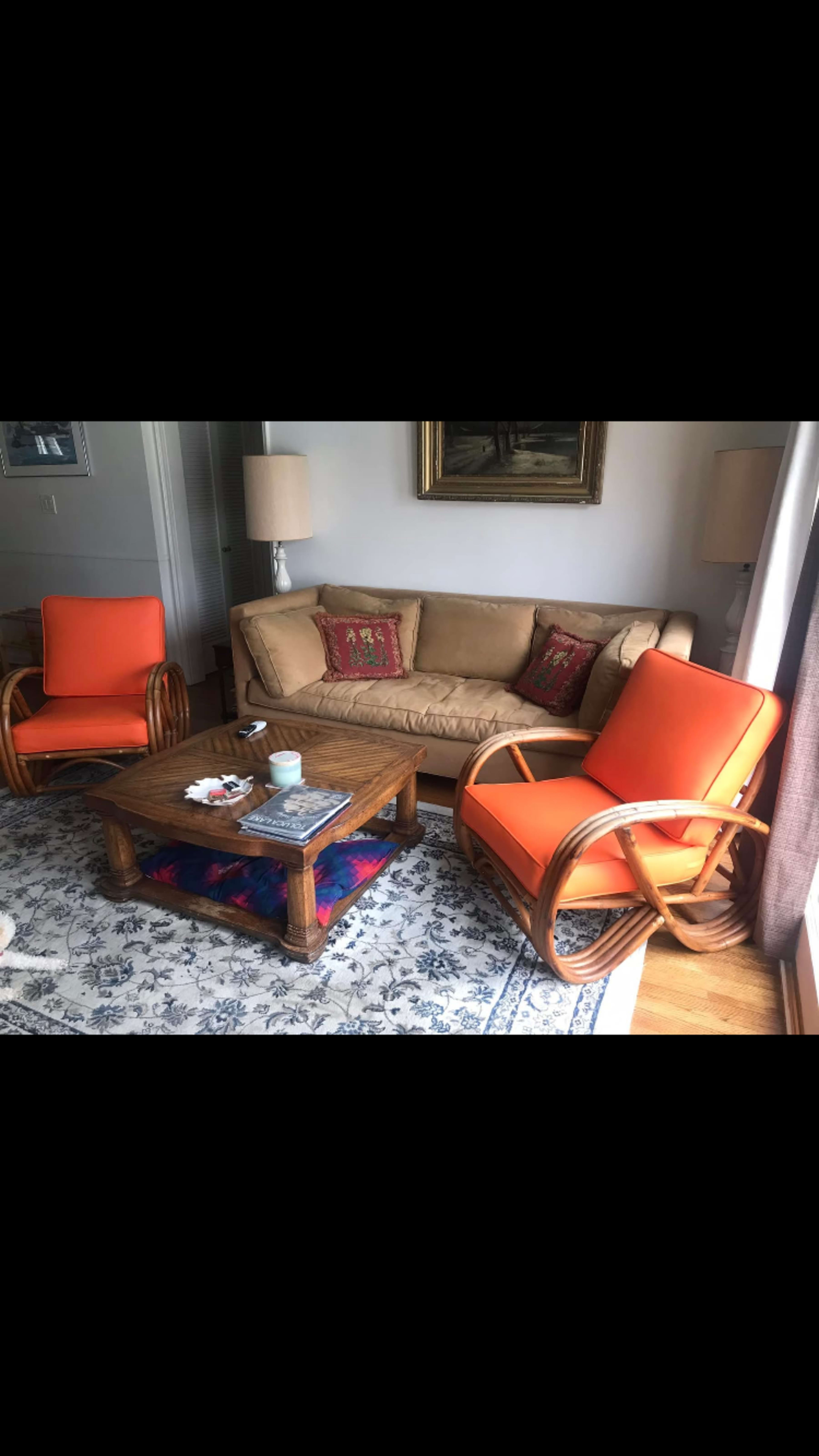 The scene shows a living room with a beige sofa, two orange rocking chairs, a wooden coffee table, and a decorative area rug.