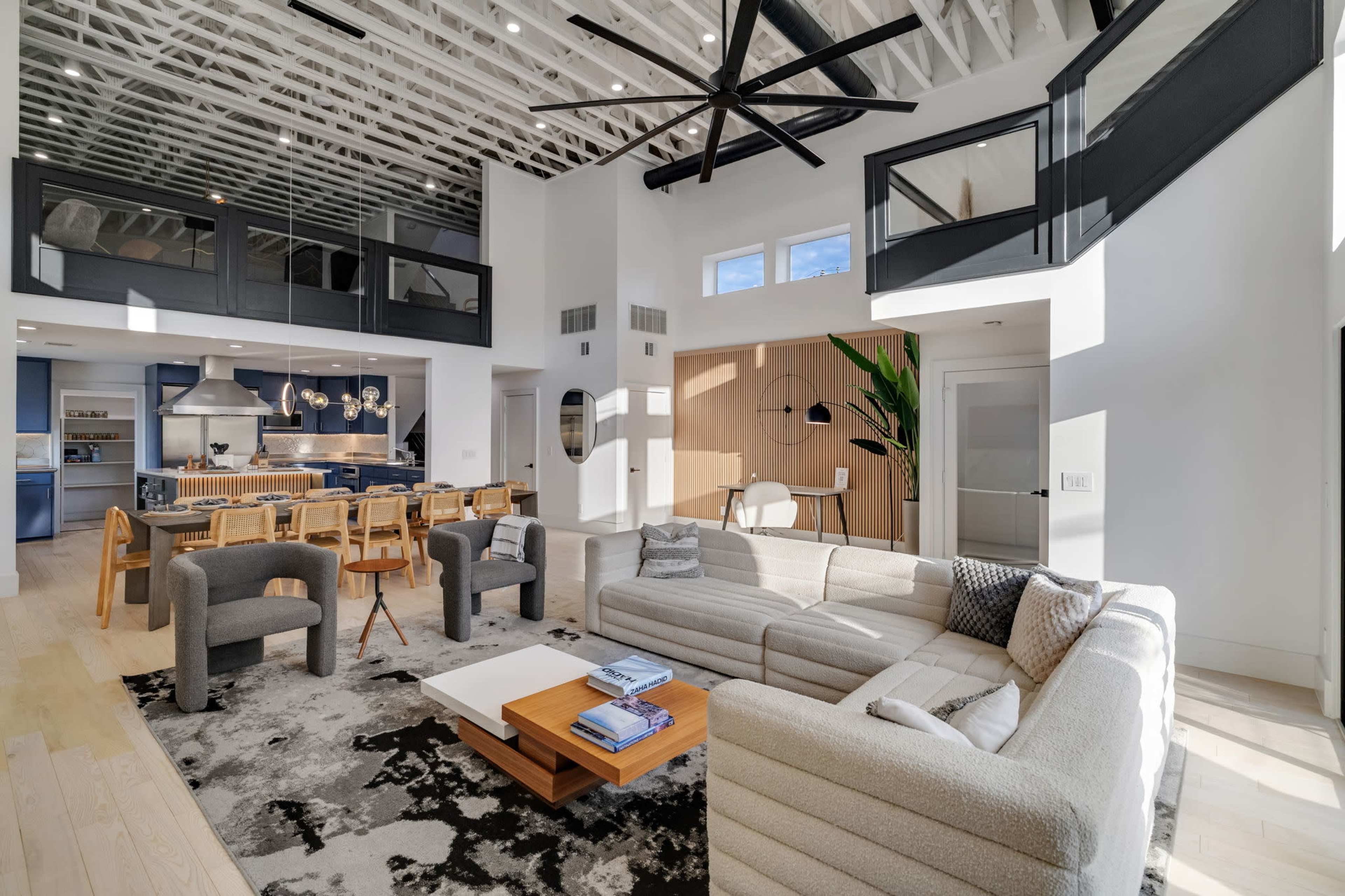 The image shows a modern living room with a large sectional sofa, a coffee table, and a view of a kitchen area with black and white cabinetry.