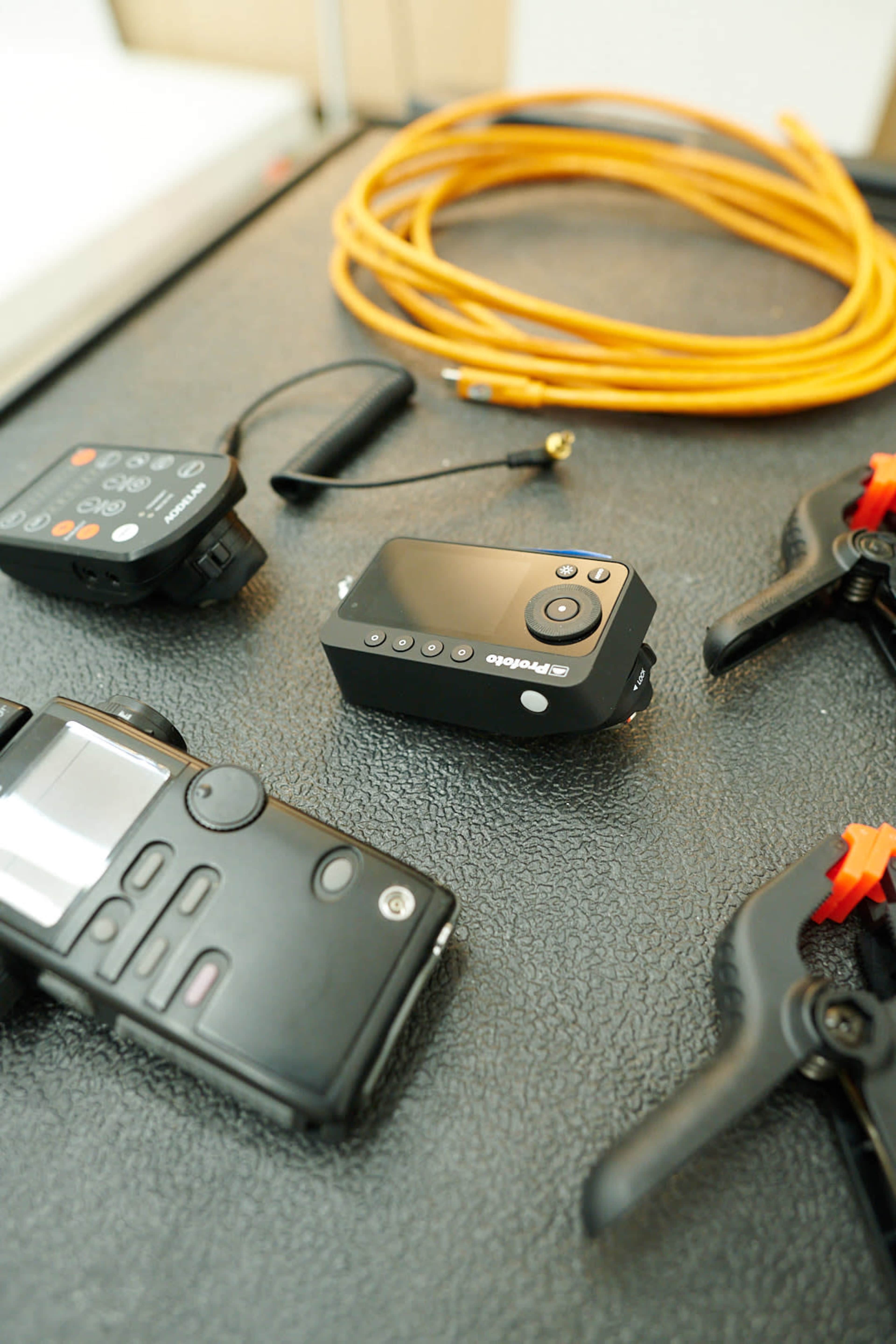 The image shows a black control device surrounded by various electronic equipment, including two handheld transmitters and a coiled orange cable.
