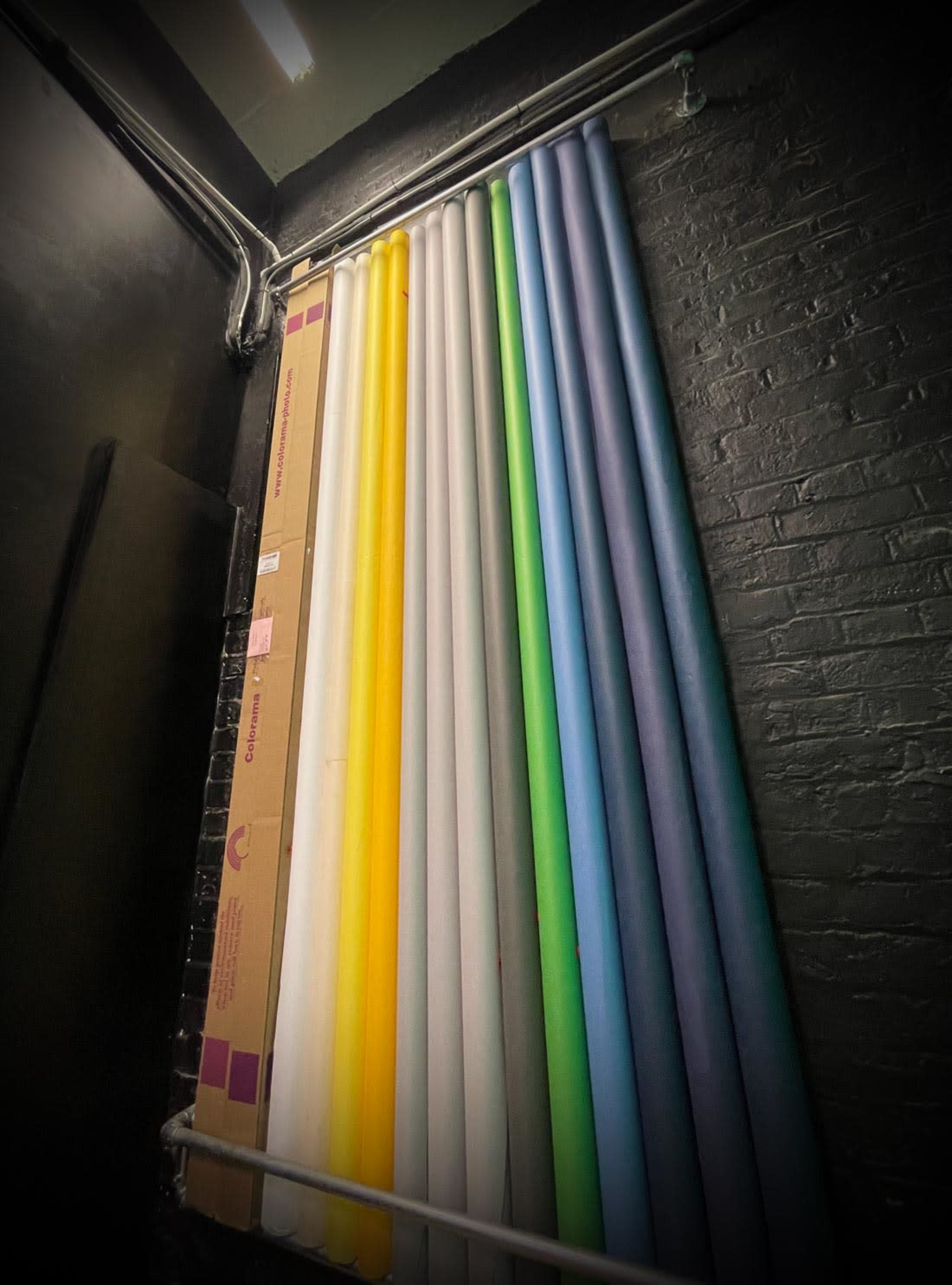 A collection of rolled paper backdrops in various colors is stored vertically against a black wall.