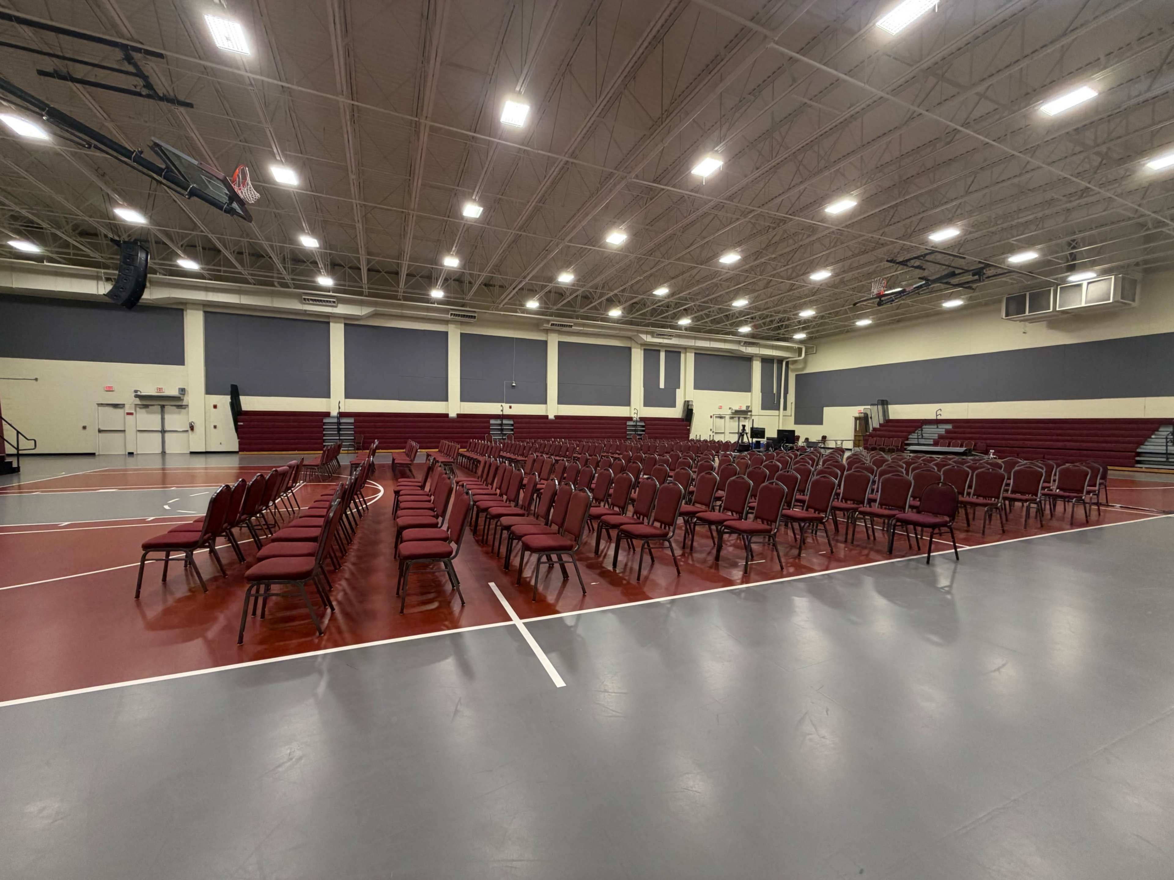 The image shows a spacious indoor venue with rows of maroon chairs arranged in a grid pattern on a gray floor.
