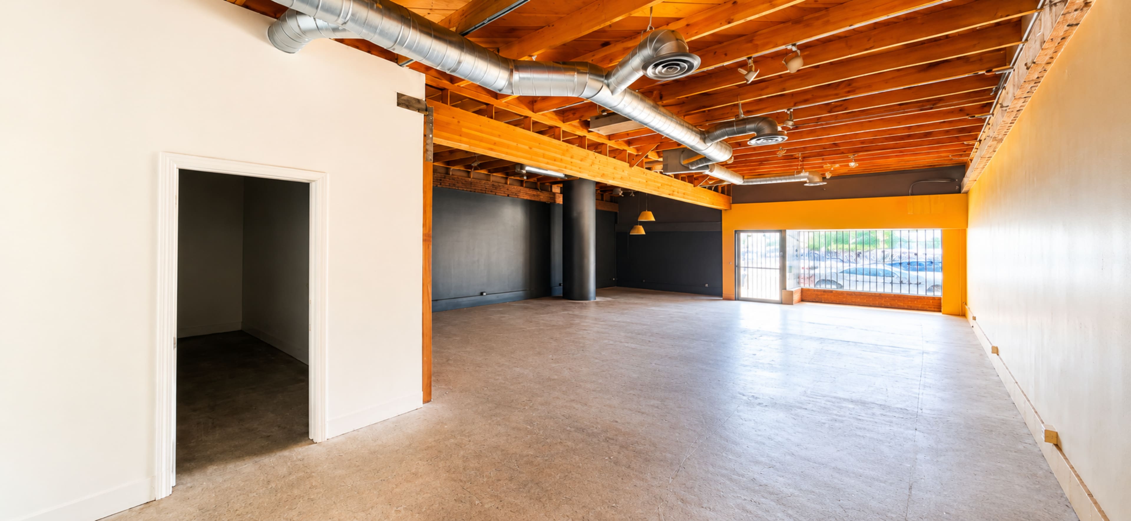 The image shows a spacious interior of a commercial building with wooden beams on the ceiling and large windows providing natural light.