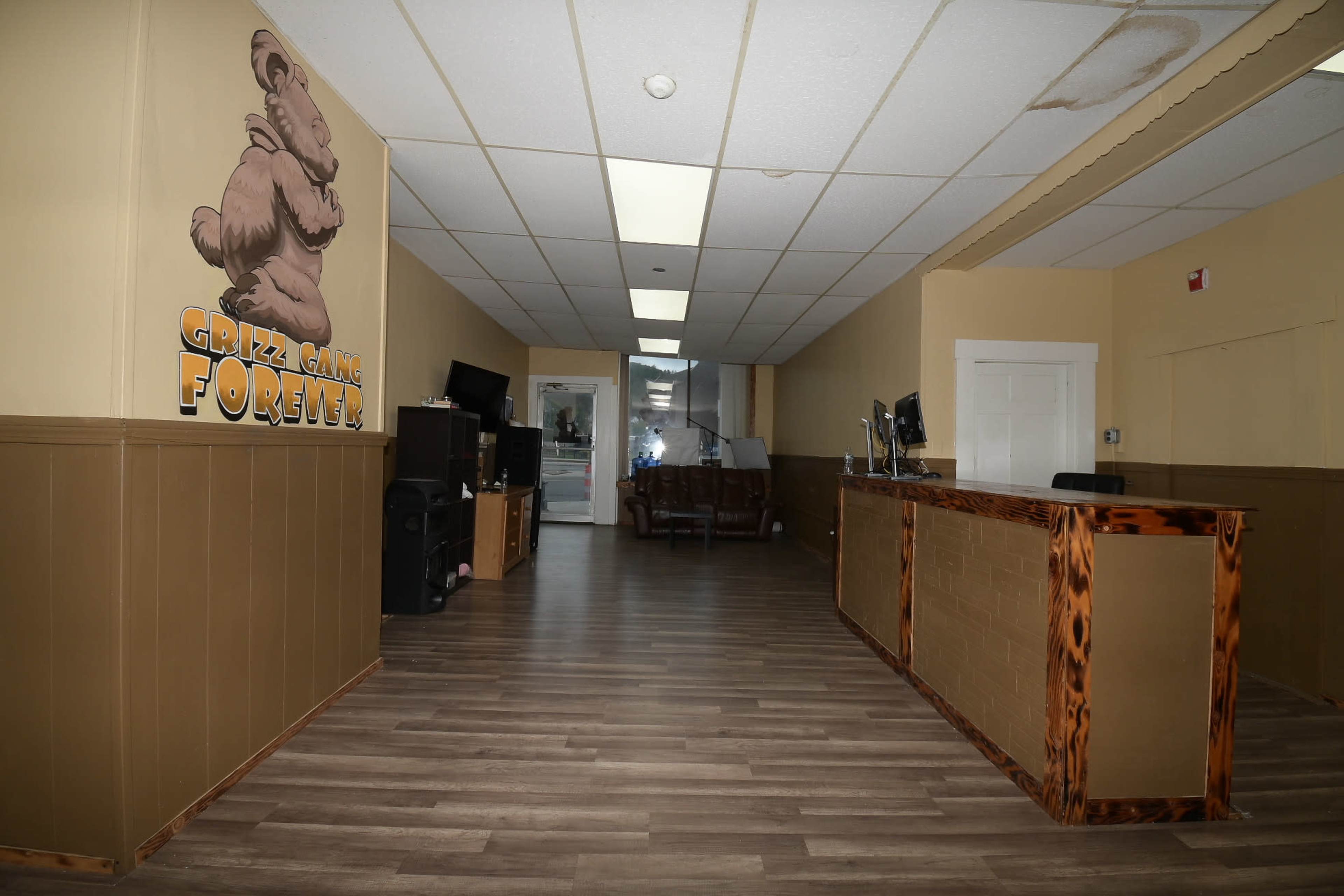 The image shows a hallway with a reception desk on the right, wooden flooring, and a cartoon bear mural on the wall.