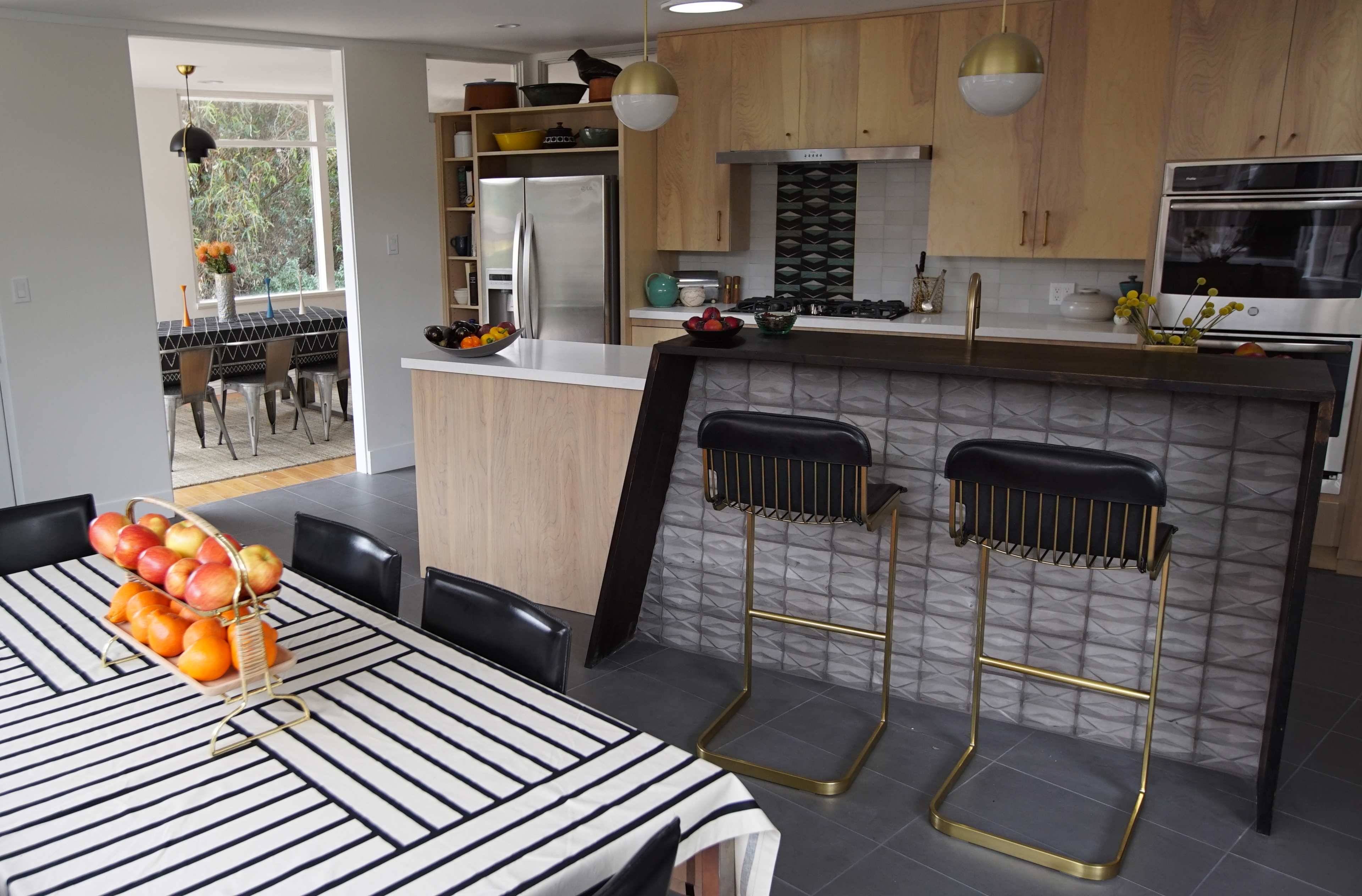 A modern kitchen features a wooden island with bar stools, a dining table set with striped linens, and stainless steel appliances.