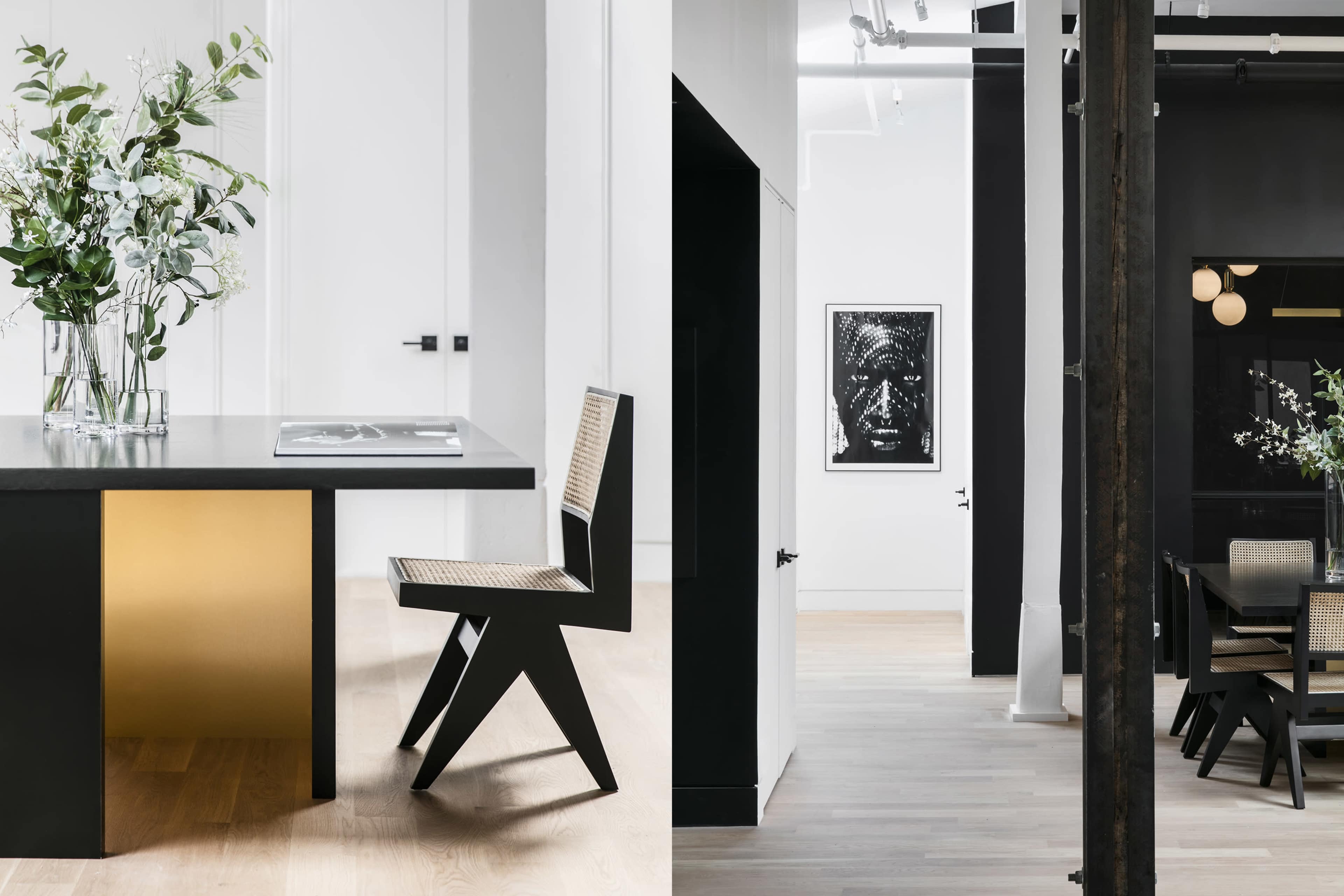 A modern kitchen with a stylish black and gold island and a minimalist chair on one side, and a spacious hallway featuring a framed artwork and light-colored wooden flooring on the other.