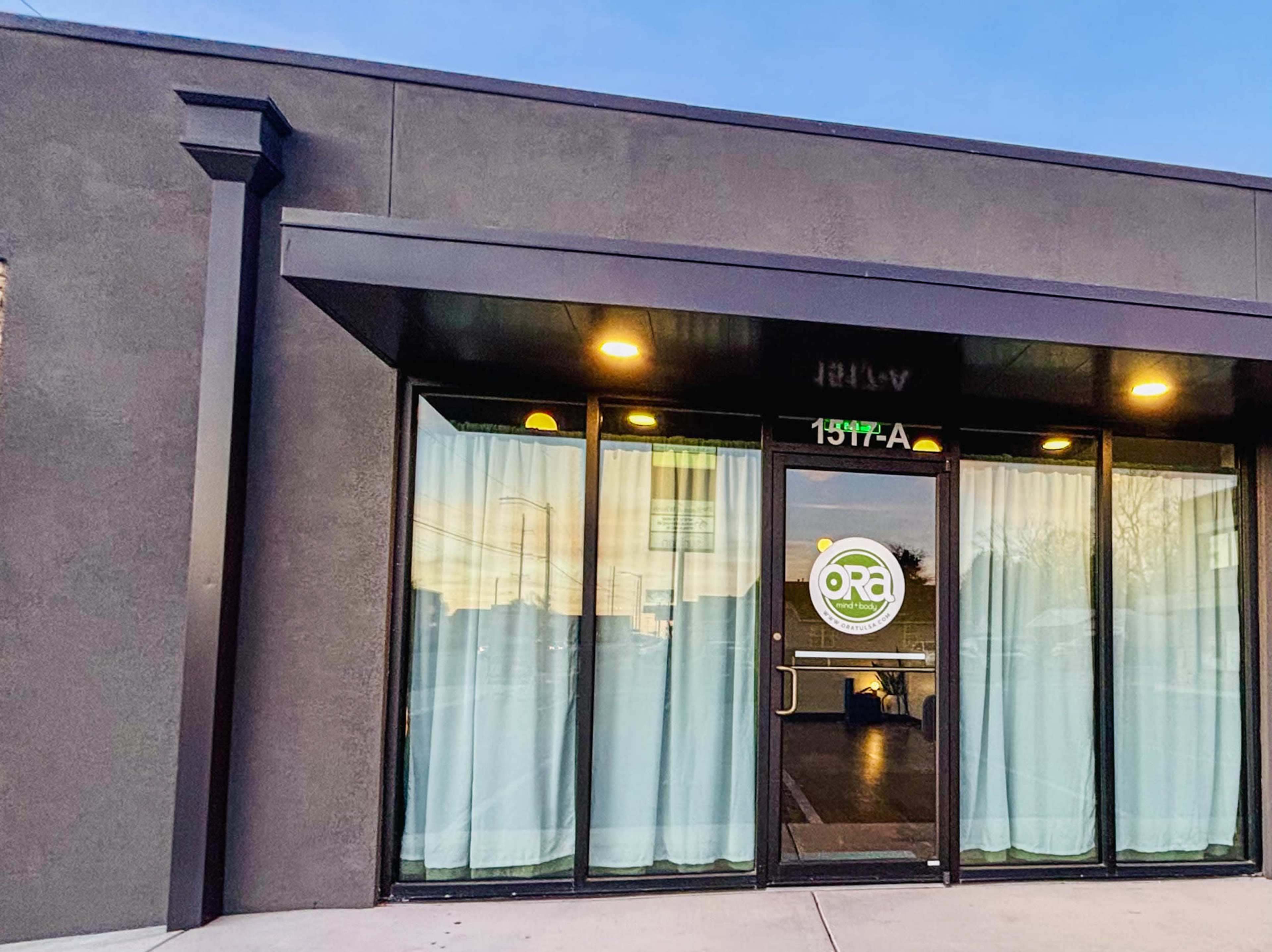 The image shows the exterior of a modern building featuring large glass doors with a circular logo and sheer curtains.