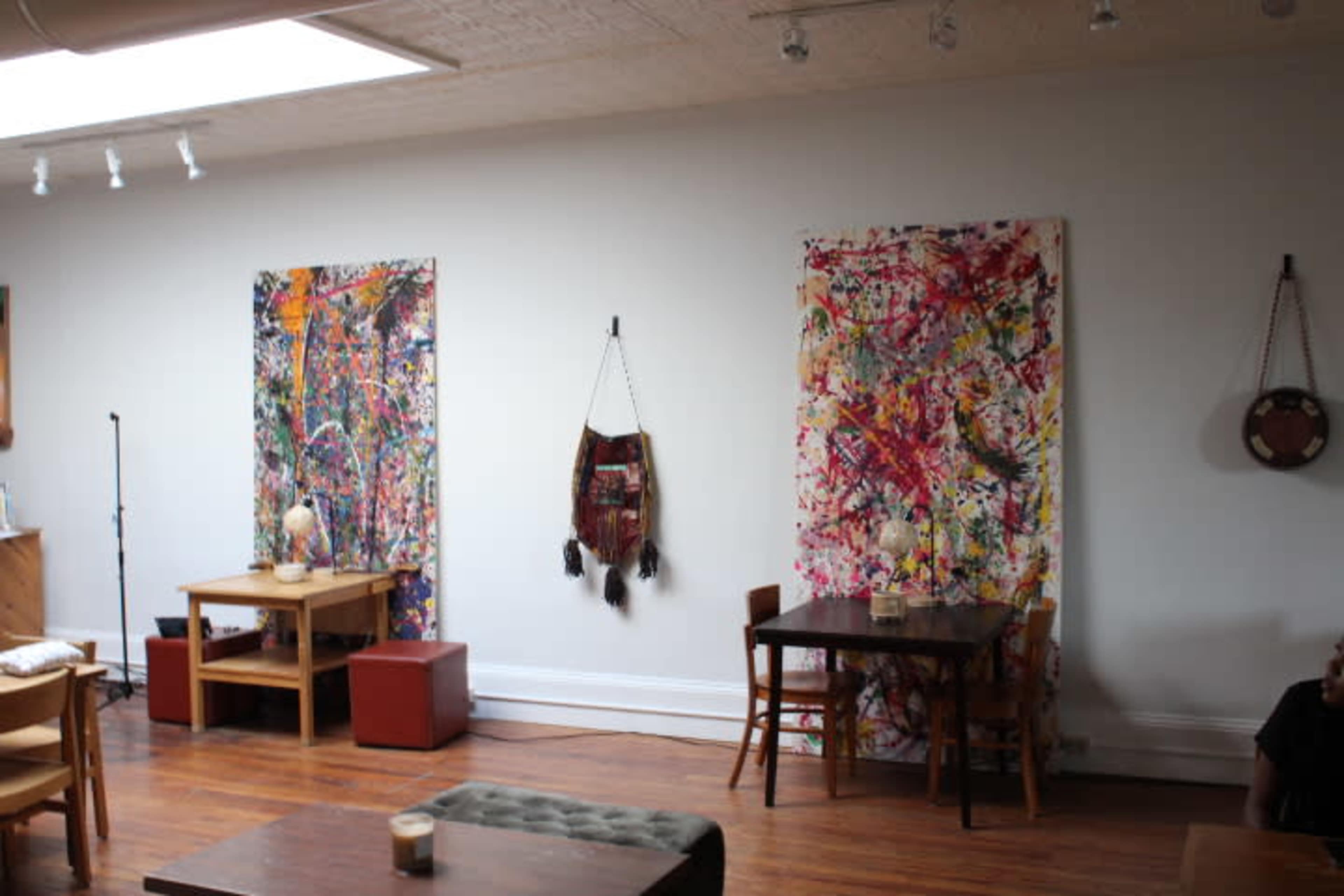 The interior of a cafe features two colorful abstract wall hangings and wooden tables arranged around a polished wooden floor.