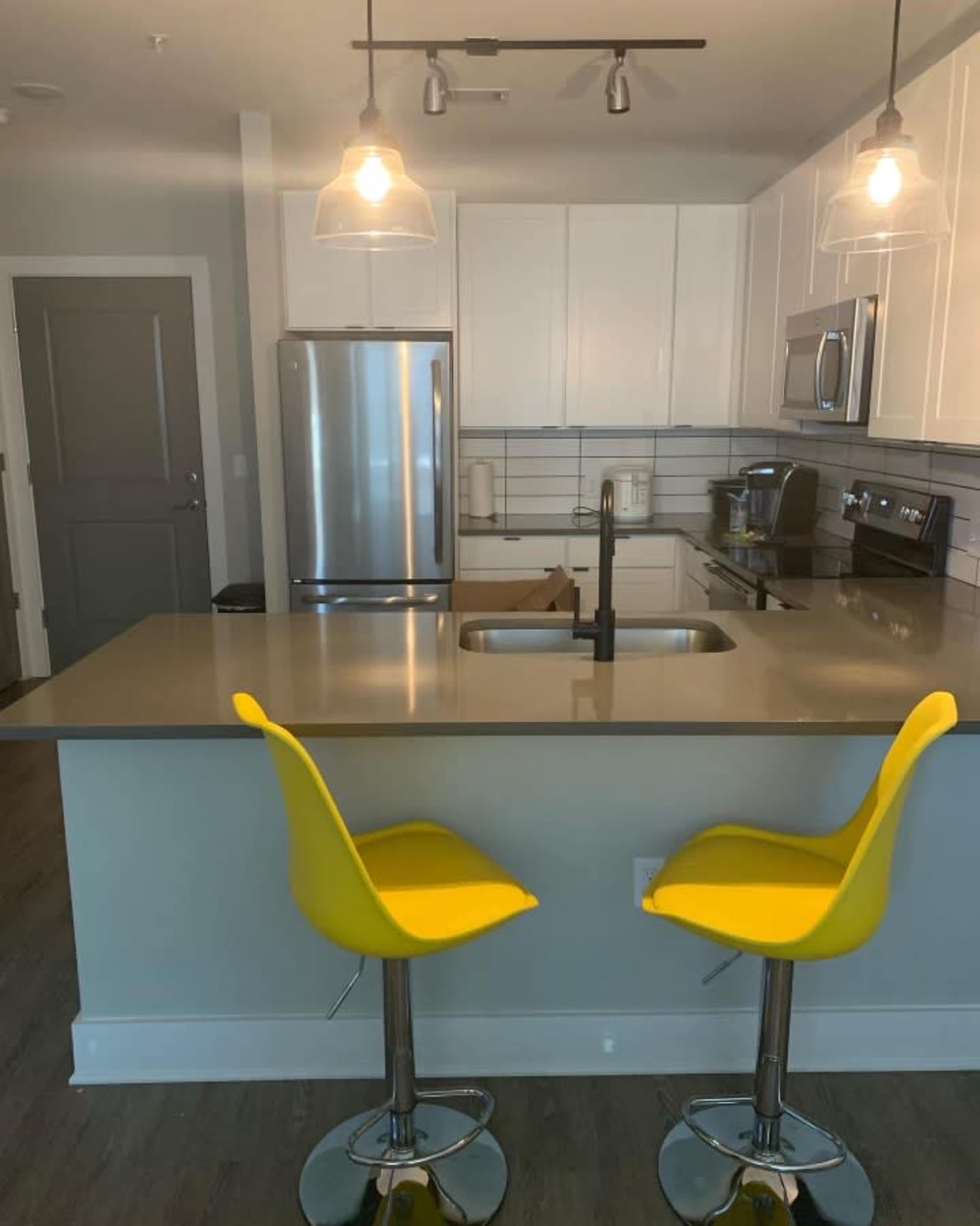 A modern kitchen features stainless steel appliances, white cabinetry, and two yellow bar stools at the island.