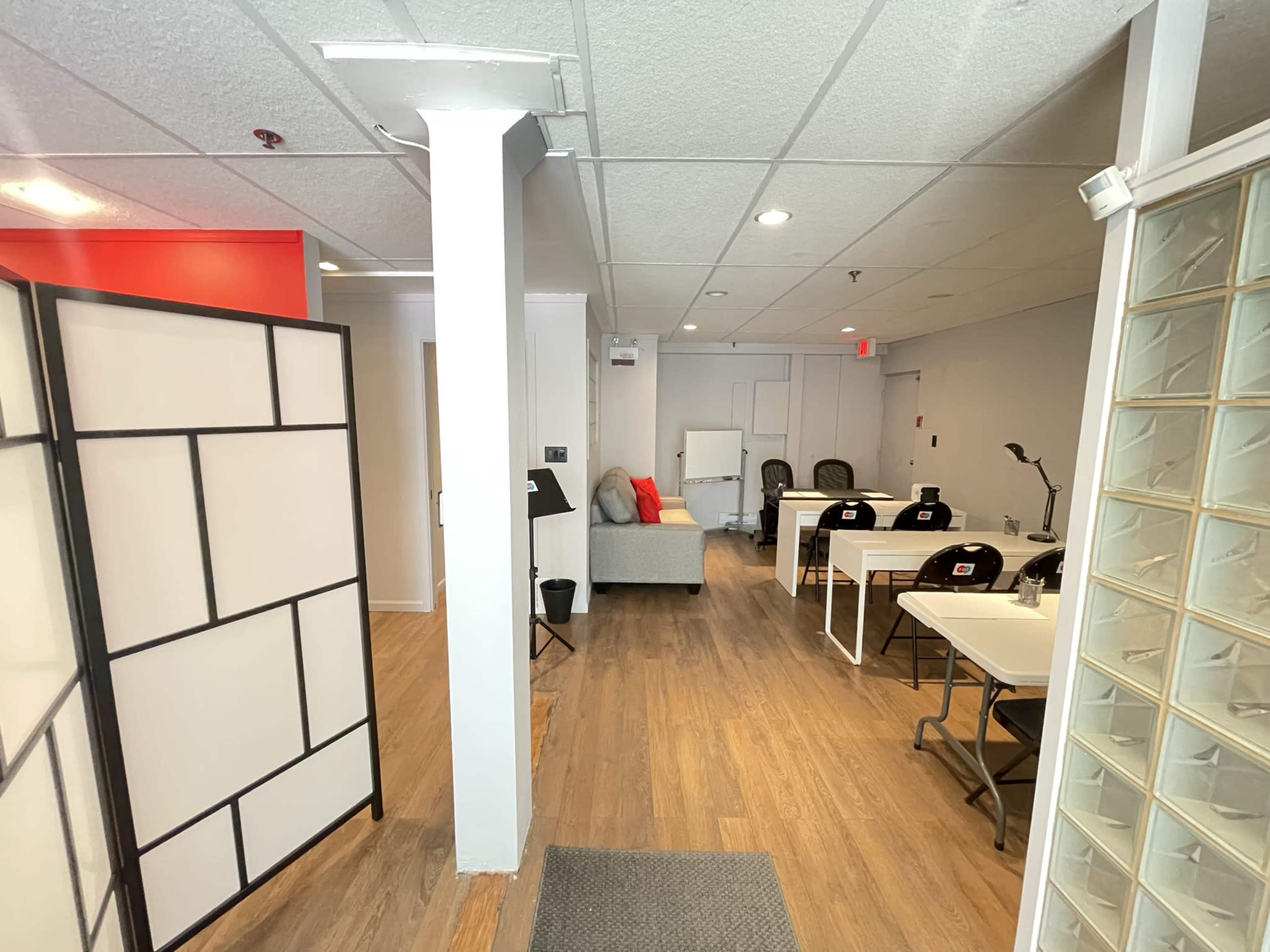 A well-lit office space features a gray sofa, several desks, and a partition with a geometric design.