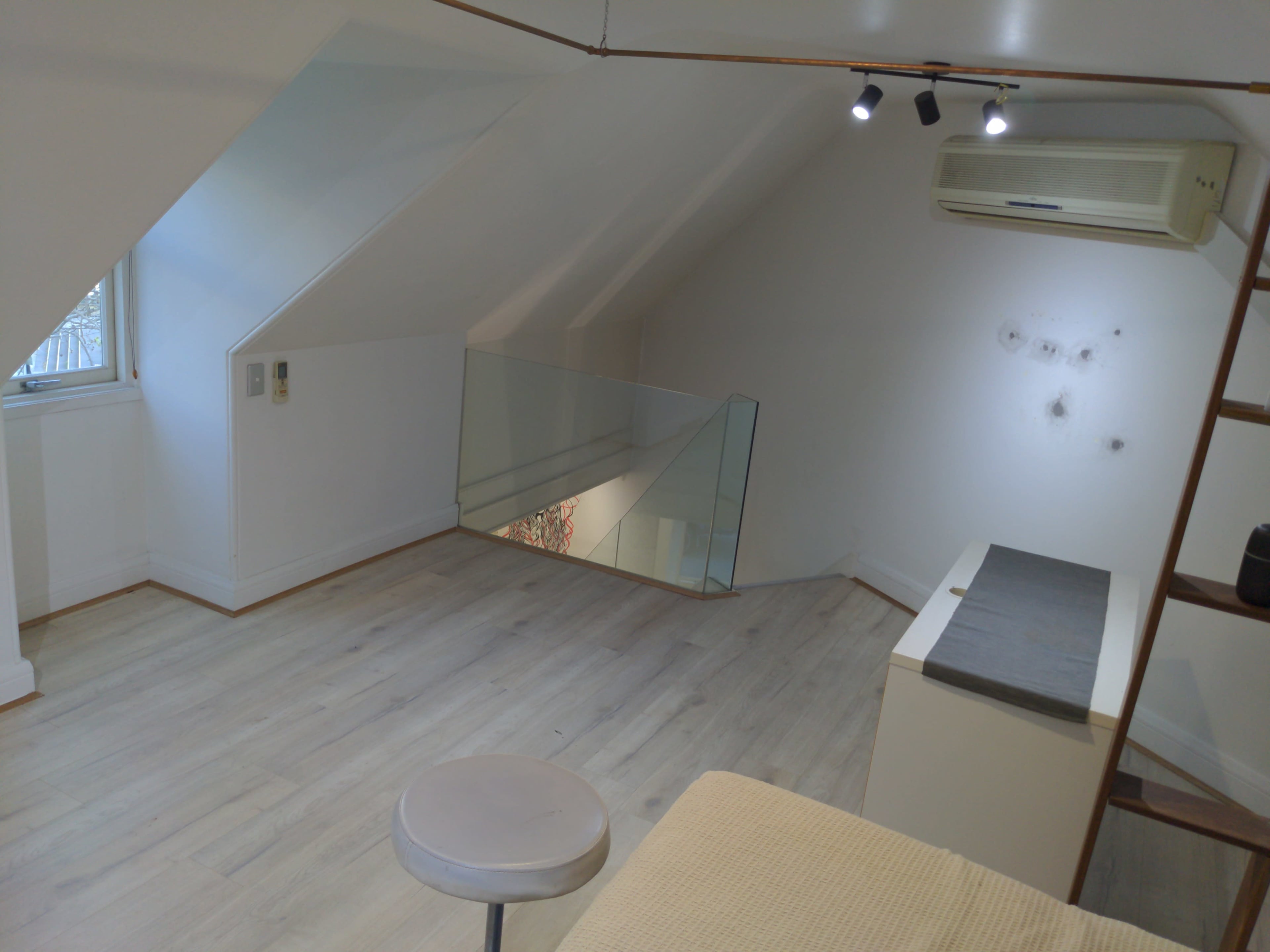 The image shows an attic room with sloped ceilings, a small stool, a mirror on the floor, and minimal furniture.