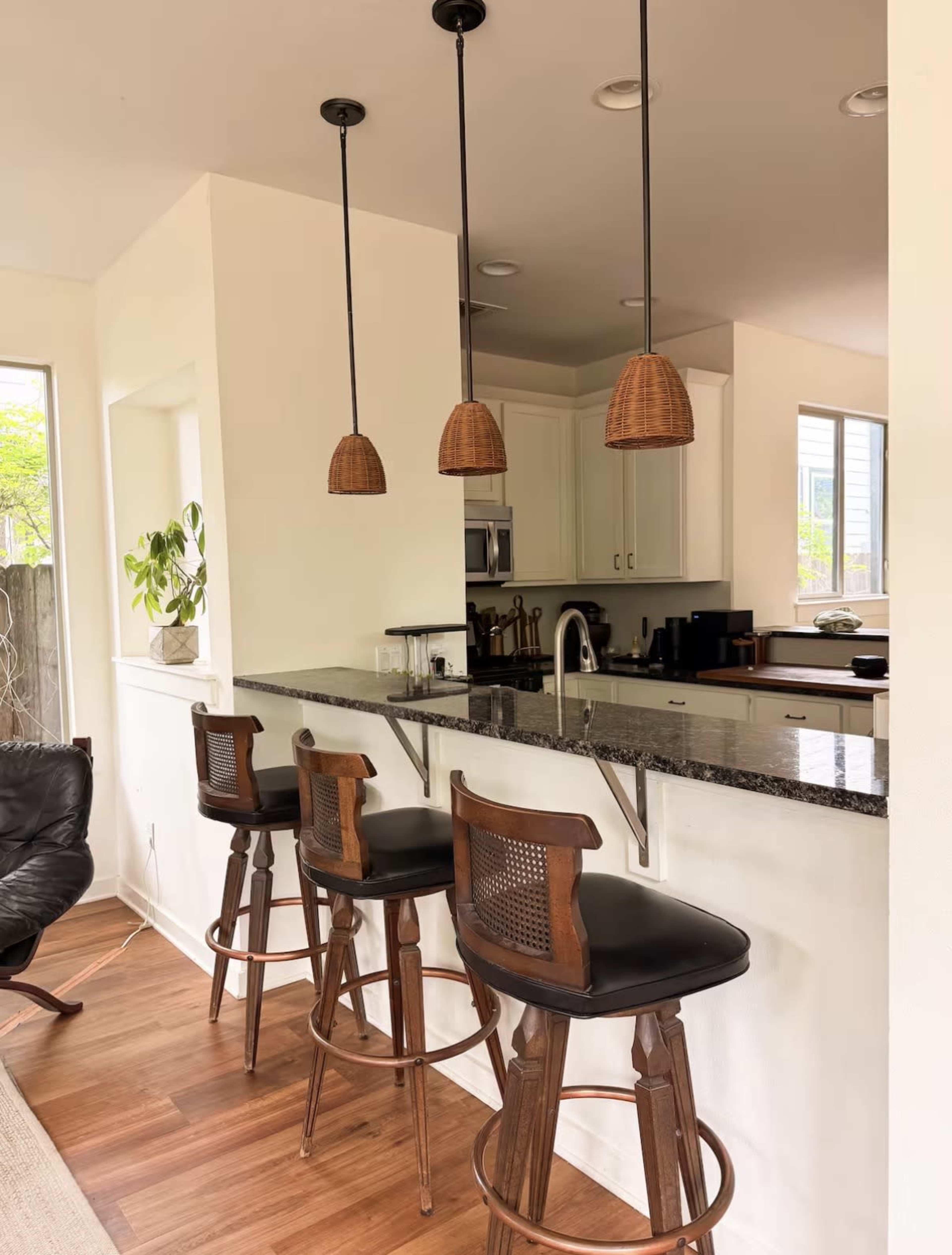 The image shows a modern kitchen with a bar counter featuring three wooden stools and three hanging pendant lights above the counter.