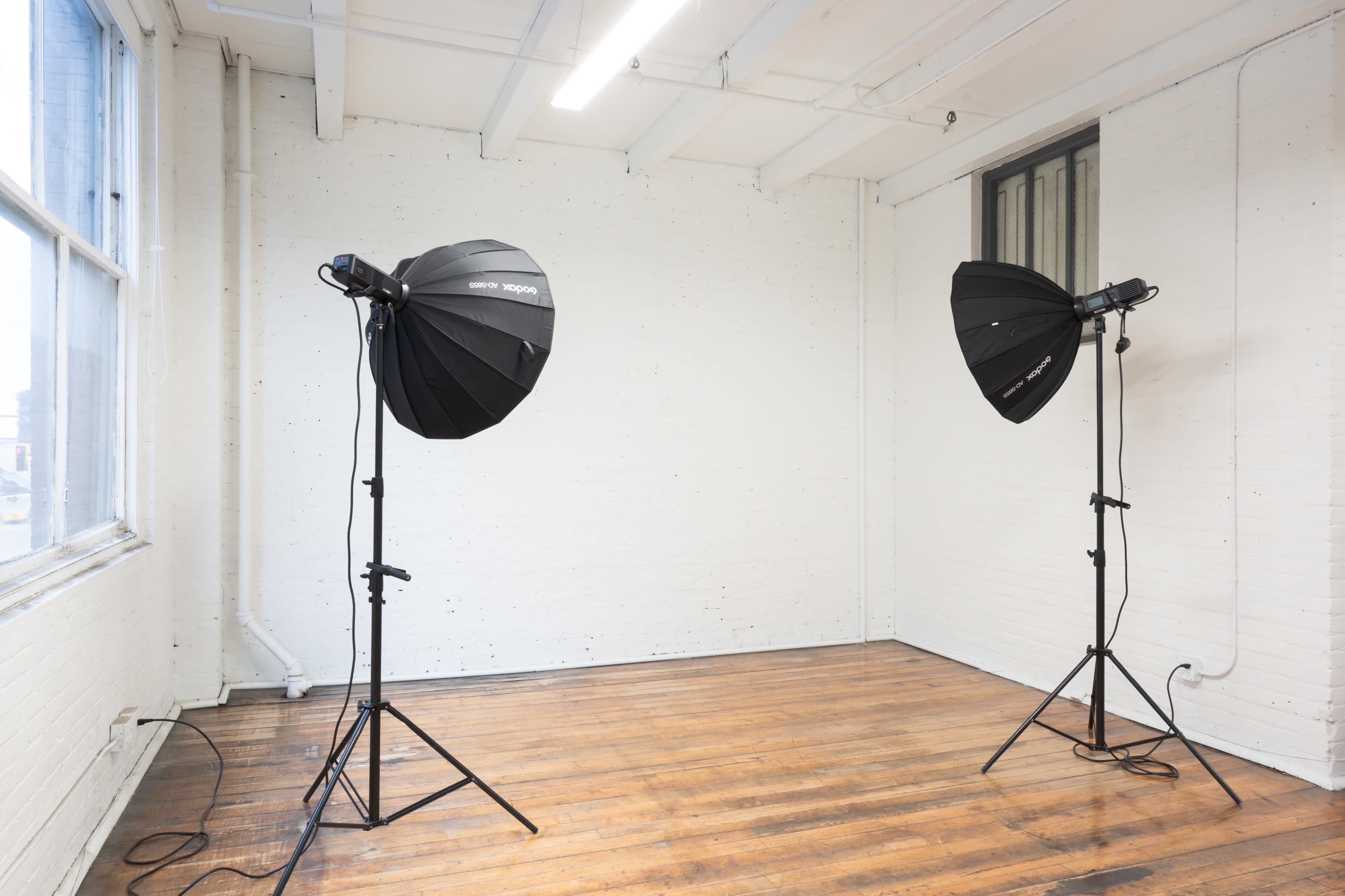 A well-lit, empty studio space with two large softboxes on tripods positioned diagonally across from each other.
