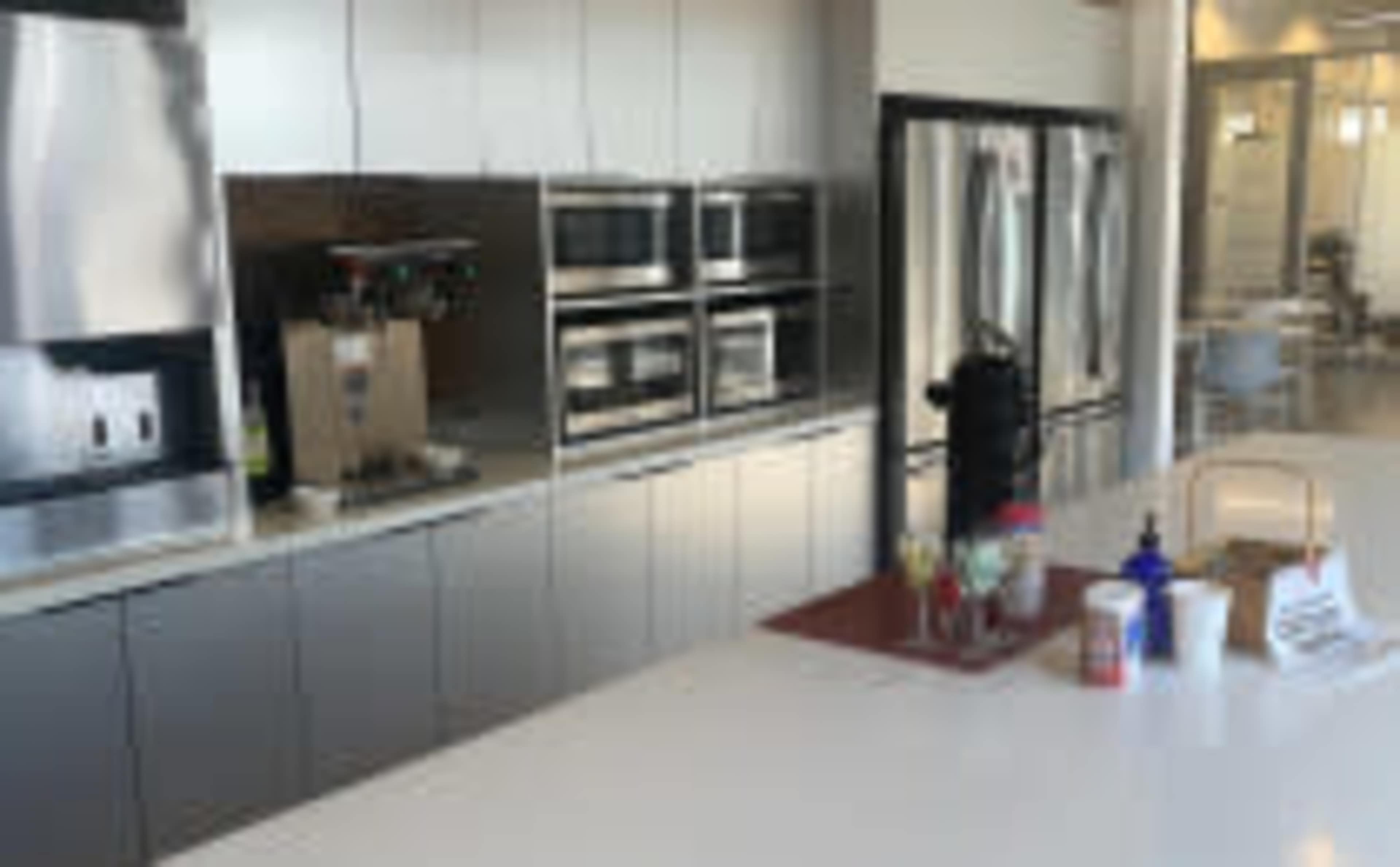 A modern kitchen with multiple stainless steel appliances, including two microwaves and three refrigerators, alongside a countertop featuring various containers and a coffee machine.