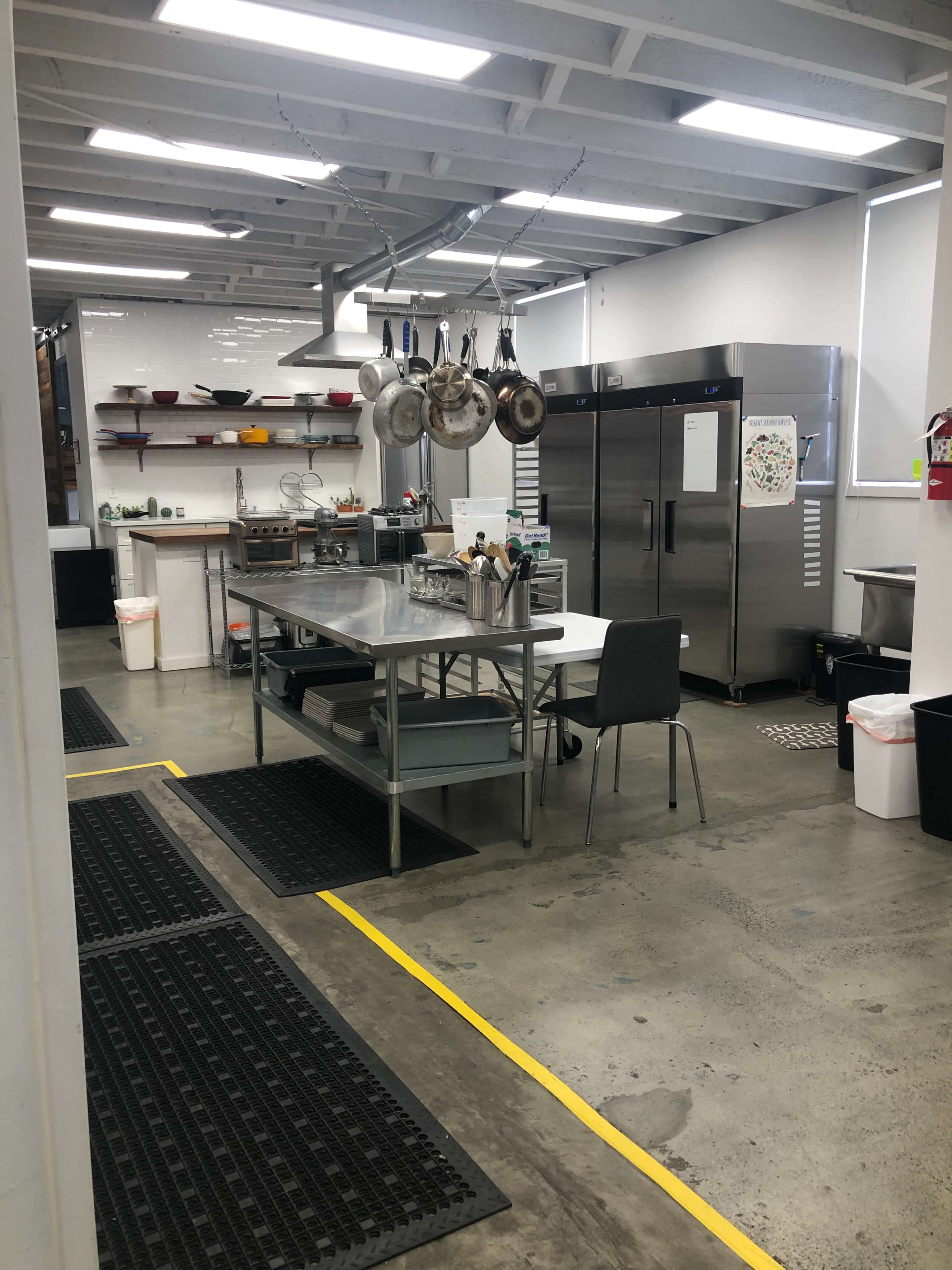 A modern kitchen equipped with stainless steel appliances, a hanging pot rack, and a central work table.