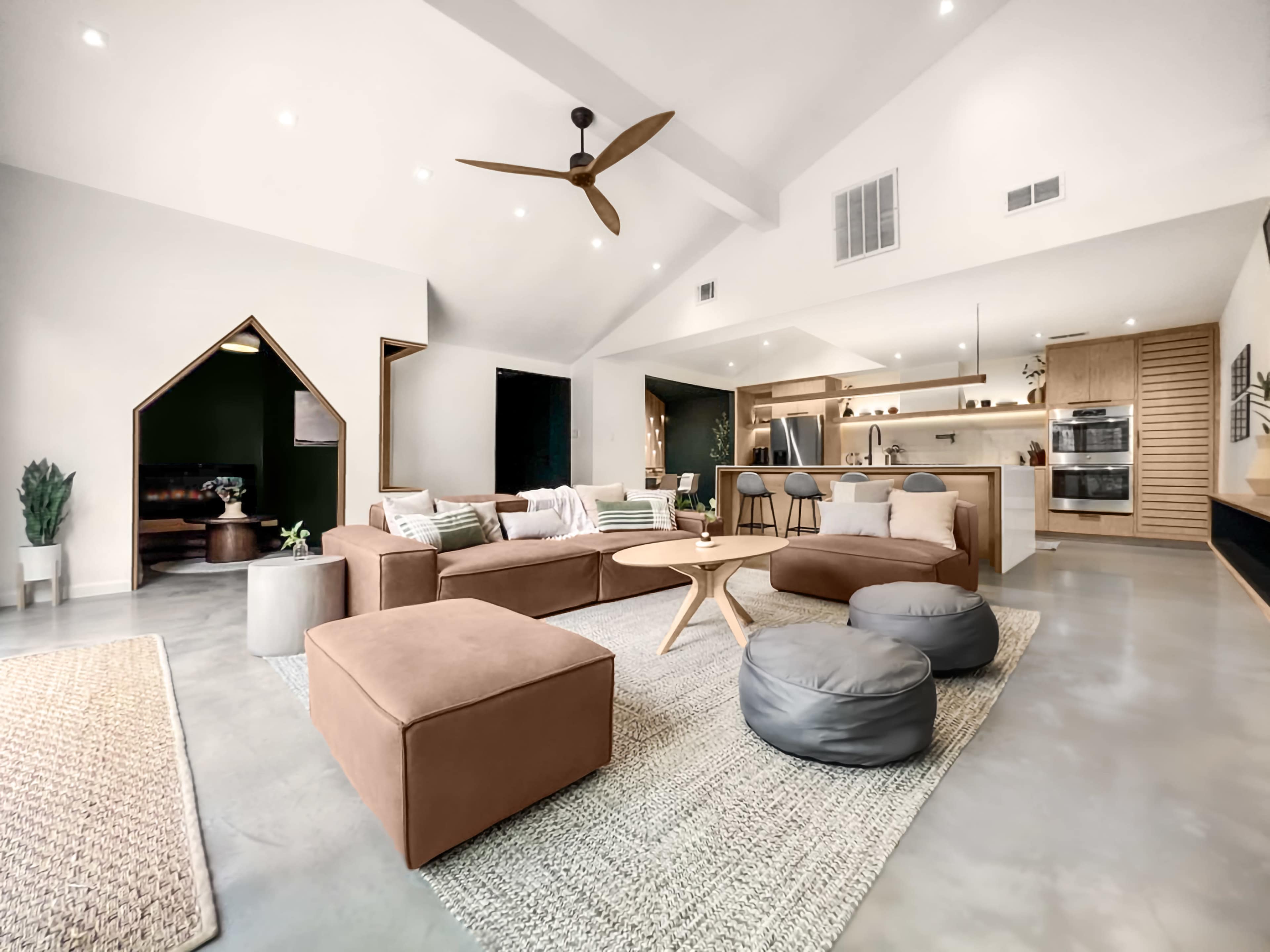 A spacious, modern living area features a large sectional sofa, a round wooden coffee table, and an open kitchen with sleek appliances.