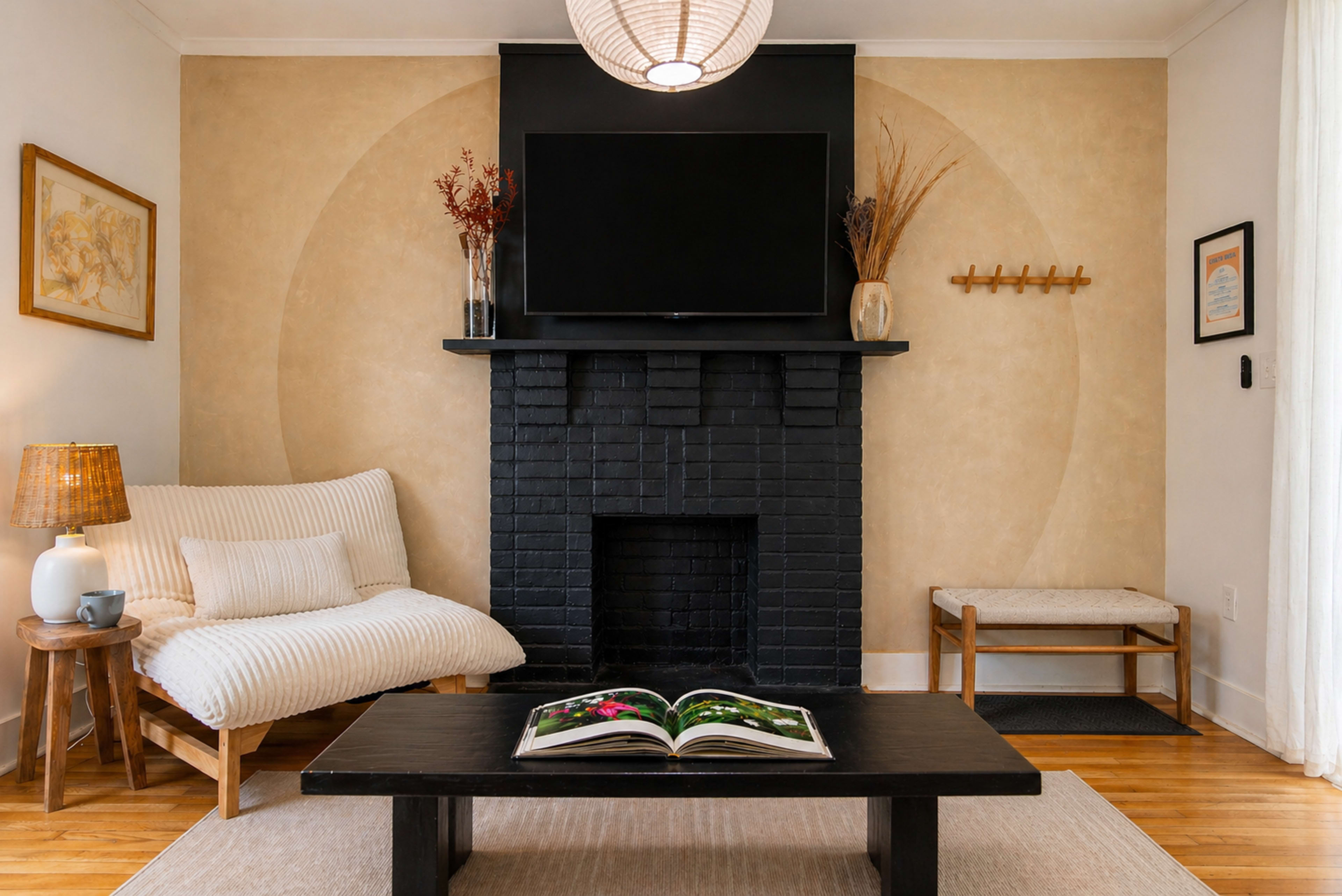 The living room features a black brick fireplace with a television mounted above it, a white sofa, a dark wooden coffee table with an open book, and decorative items on the walls and shelves.