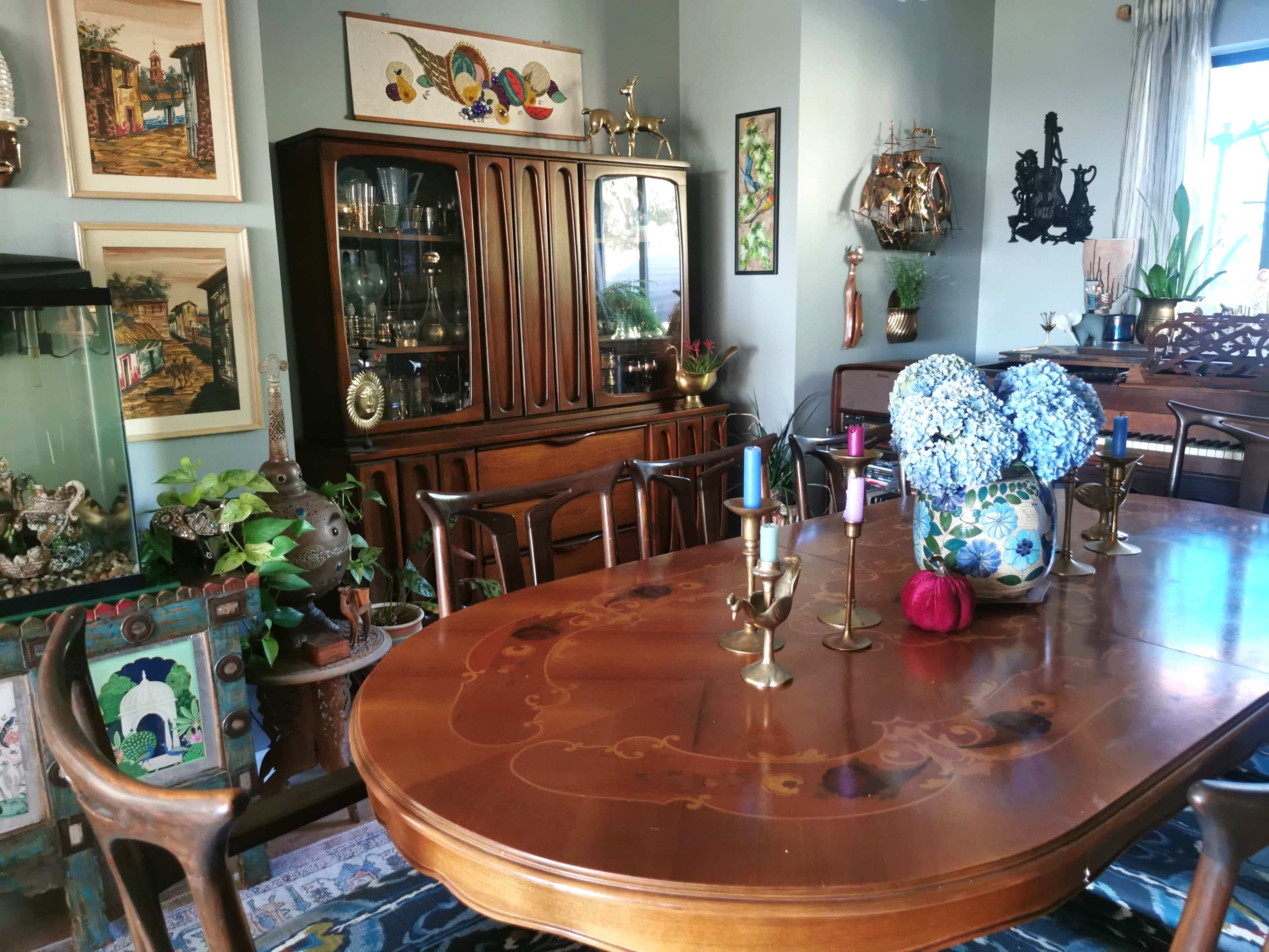 A polished wooden dining table with decorative candlesticks and a floral centerpiece is surrounded by antique furniture in a well-decorated room.