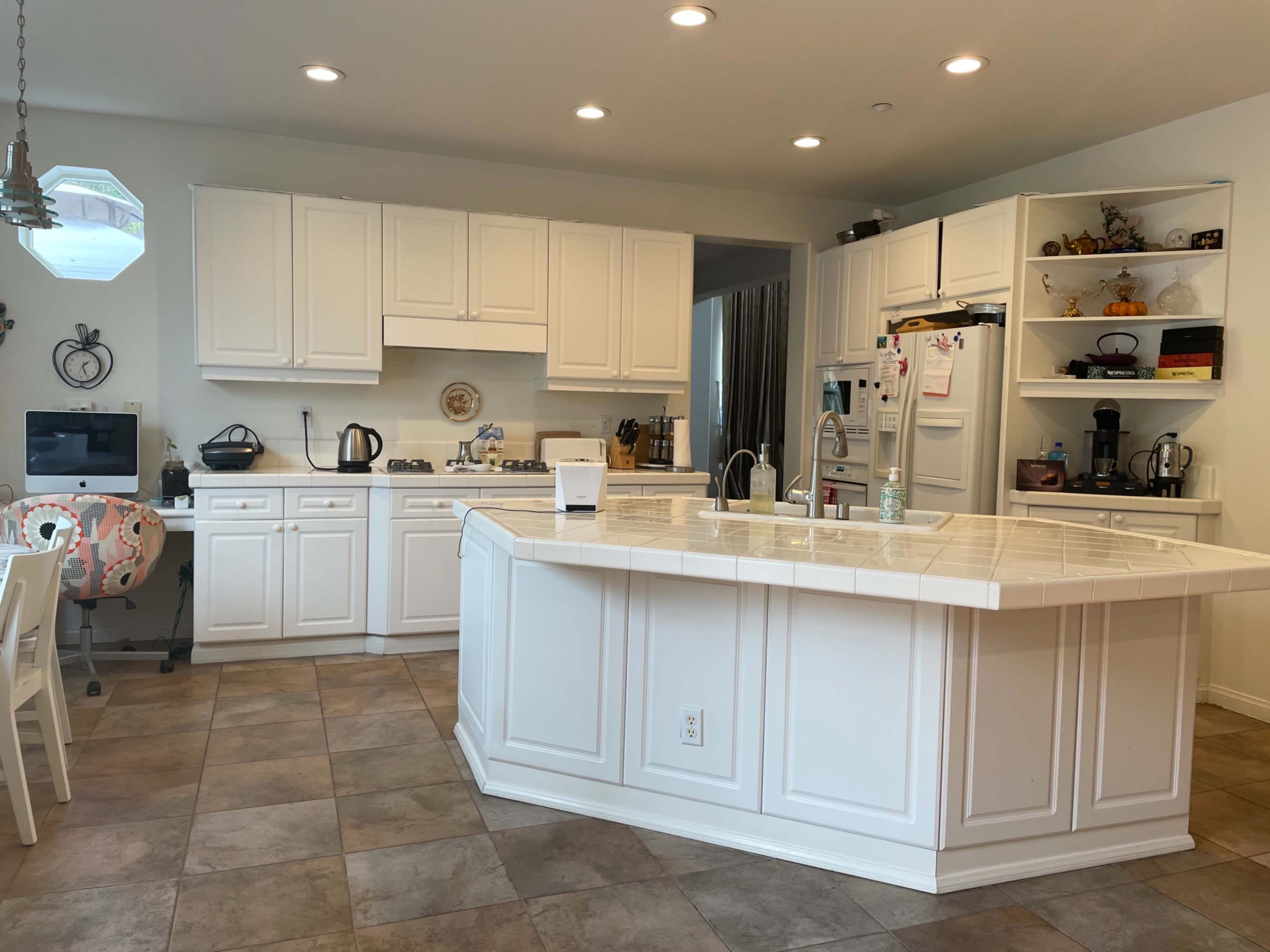 The kitchen features white cabinets, a tiled countertop with a central island, and several appliances arranged throughout the space.