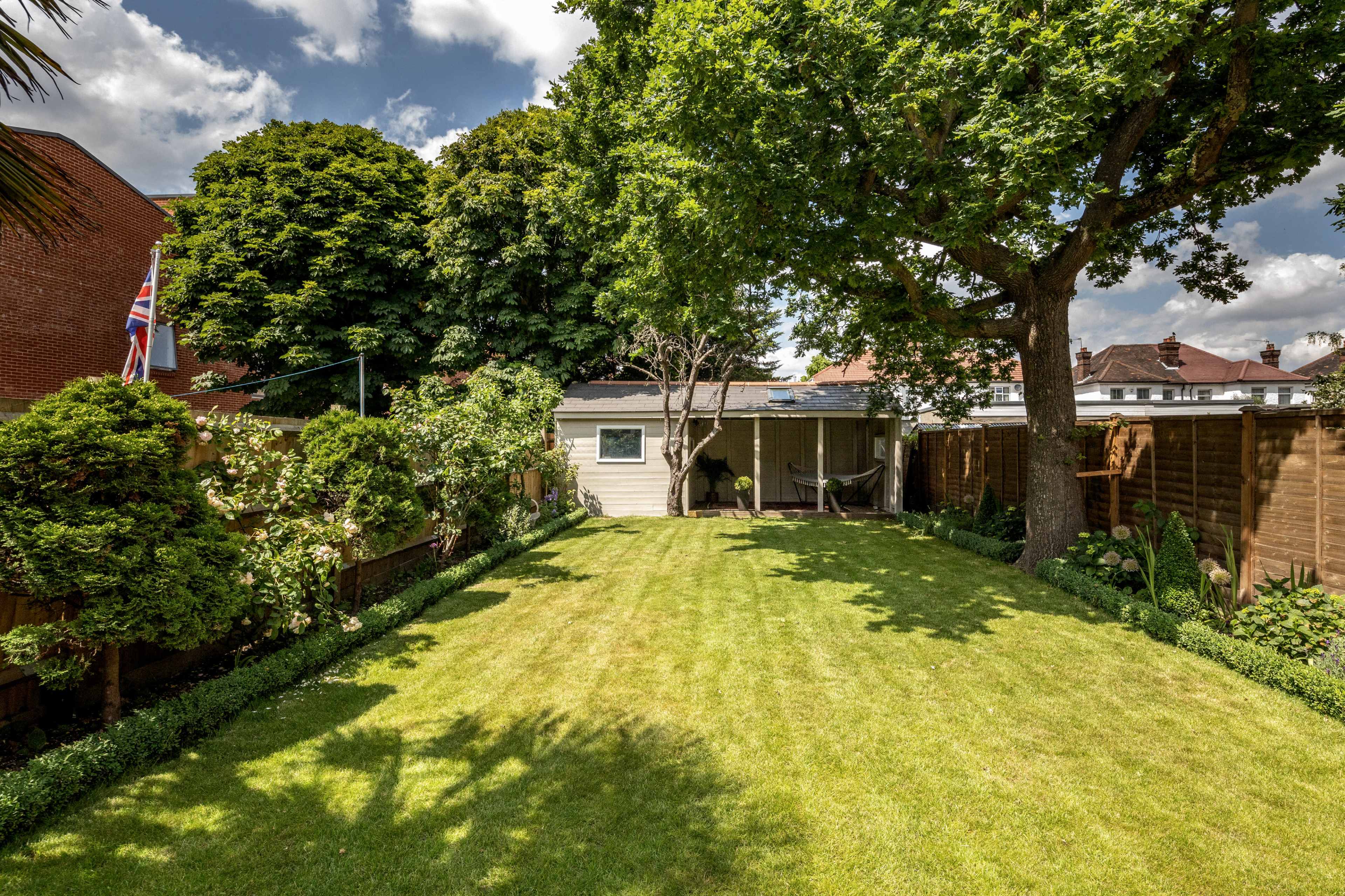 A well-manicured garden featuring a grassy lawn, shrubs, and a small shed, with a flagpole displaying the Union Jack.