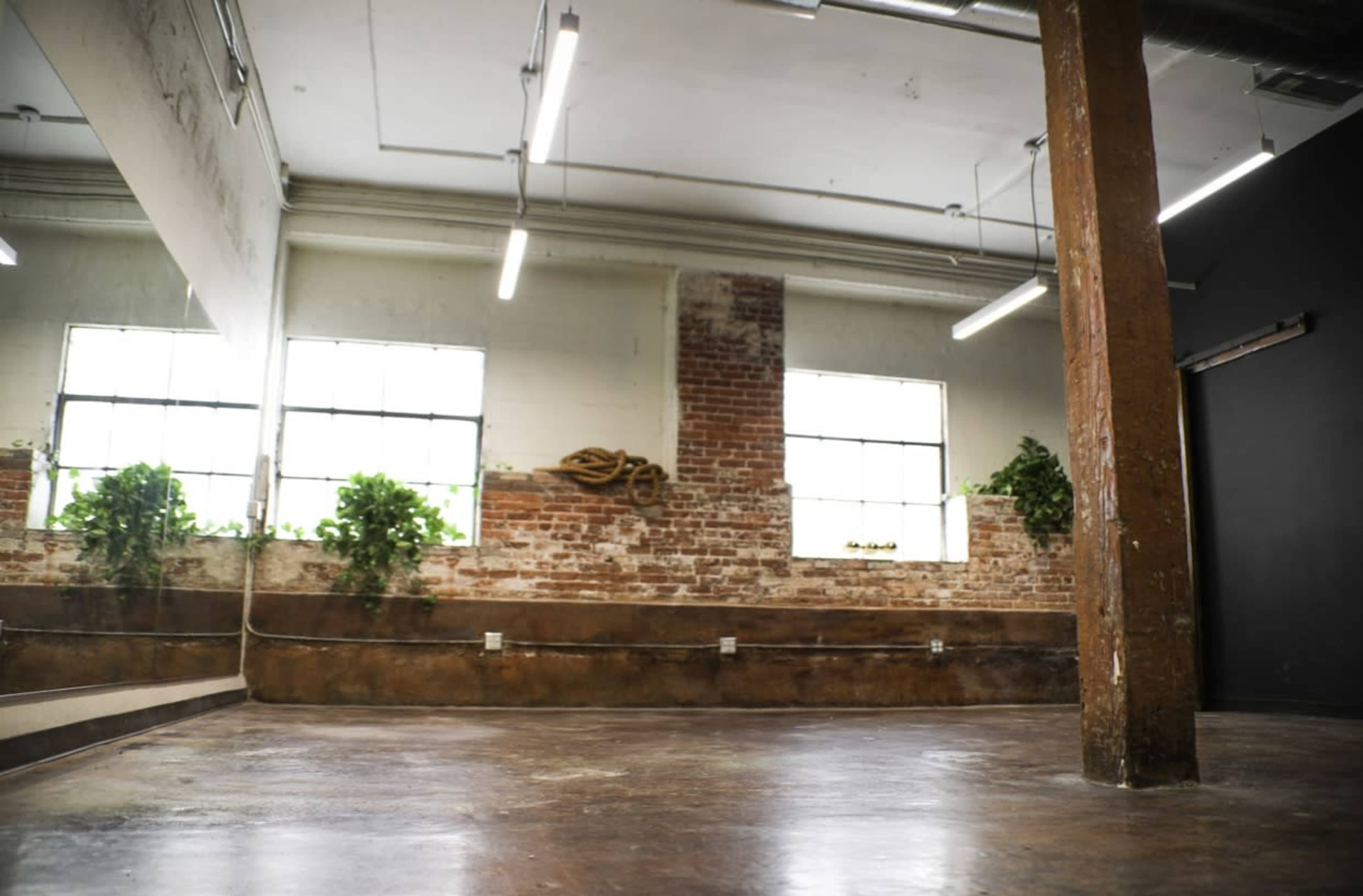 An empty studio space with exposed brick walls, large windows, and polished concrete flooring.