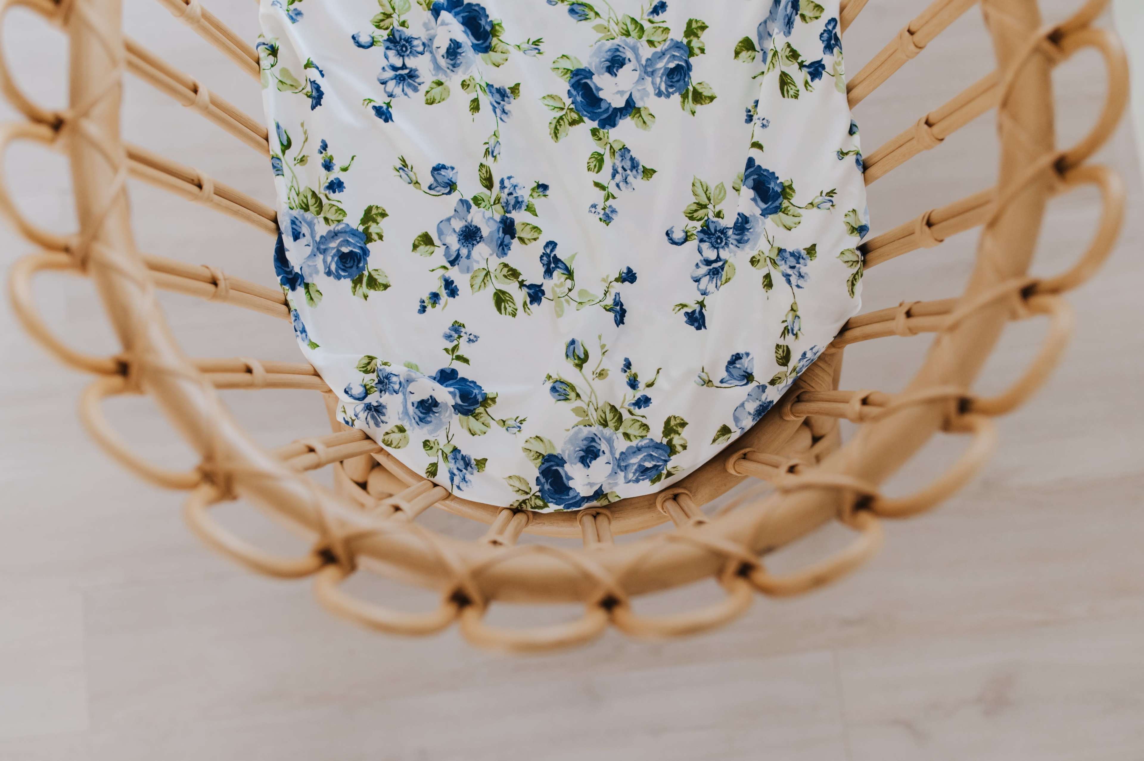 A circular woven bassinet with a floral-patterned sheet resting inside.