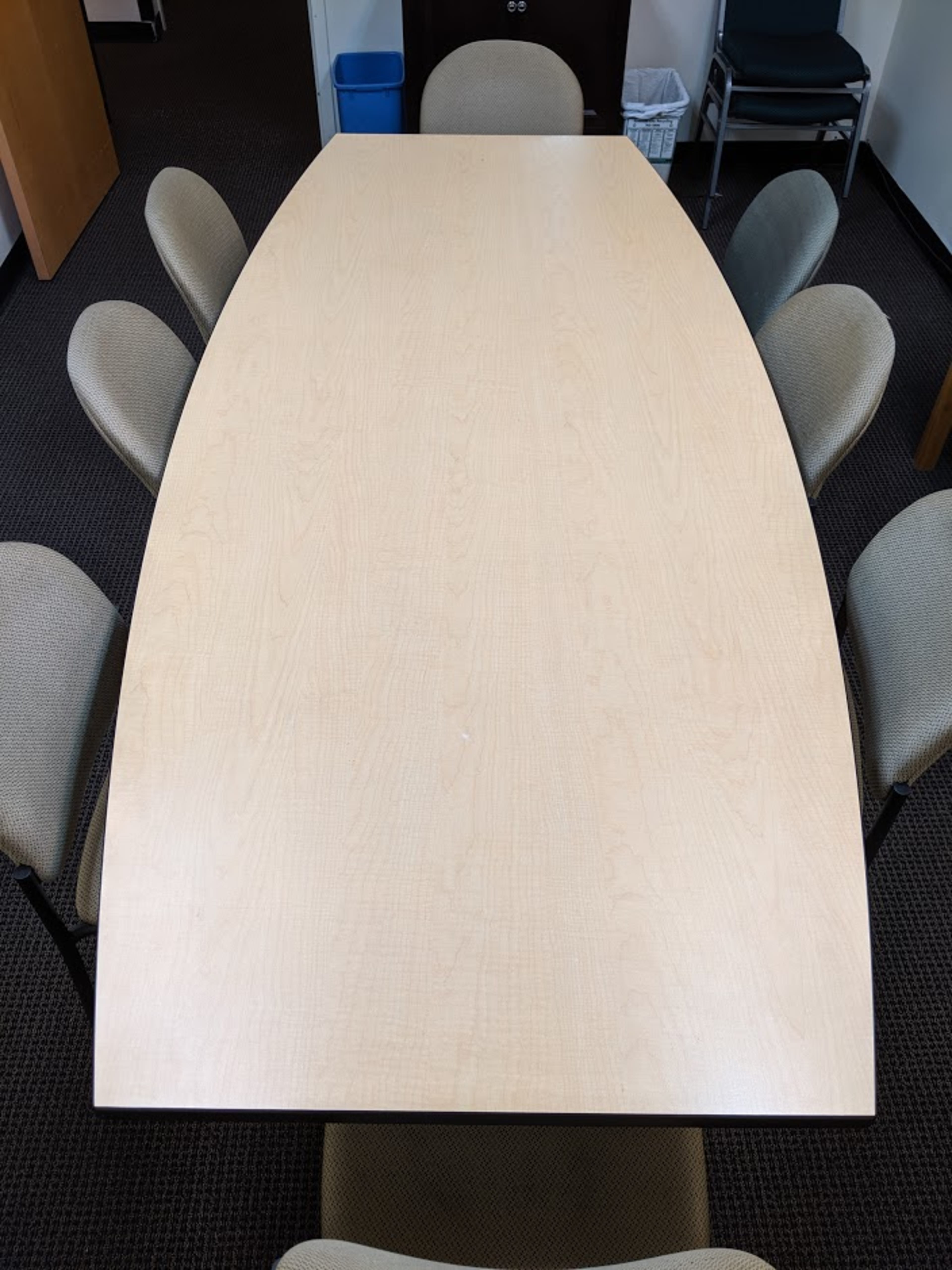 A rectangular table with eight surrounding chairs is positioned in a room with carpeted flooring and office furnishings.