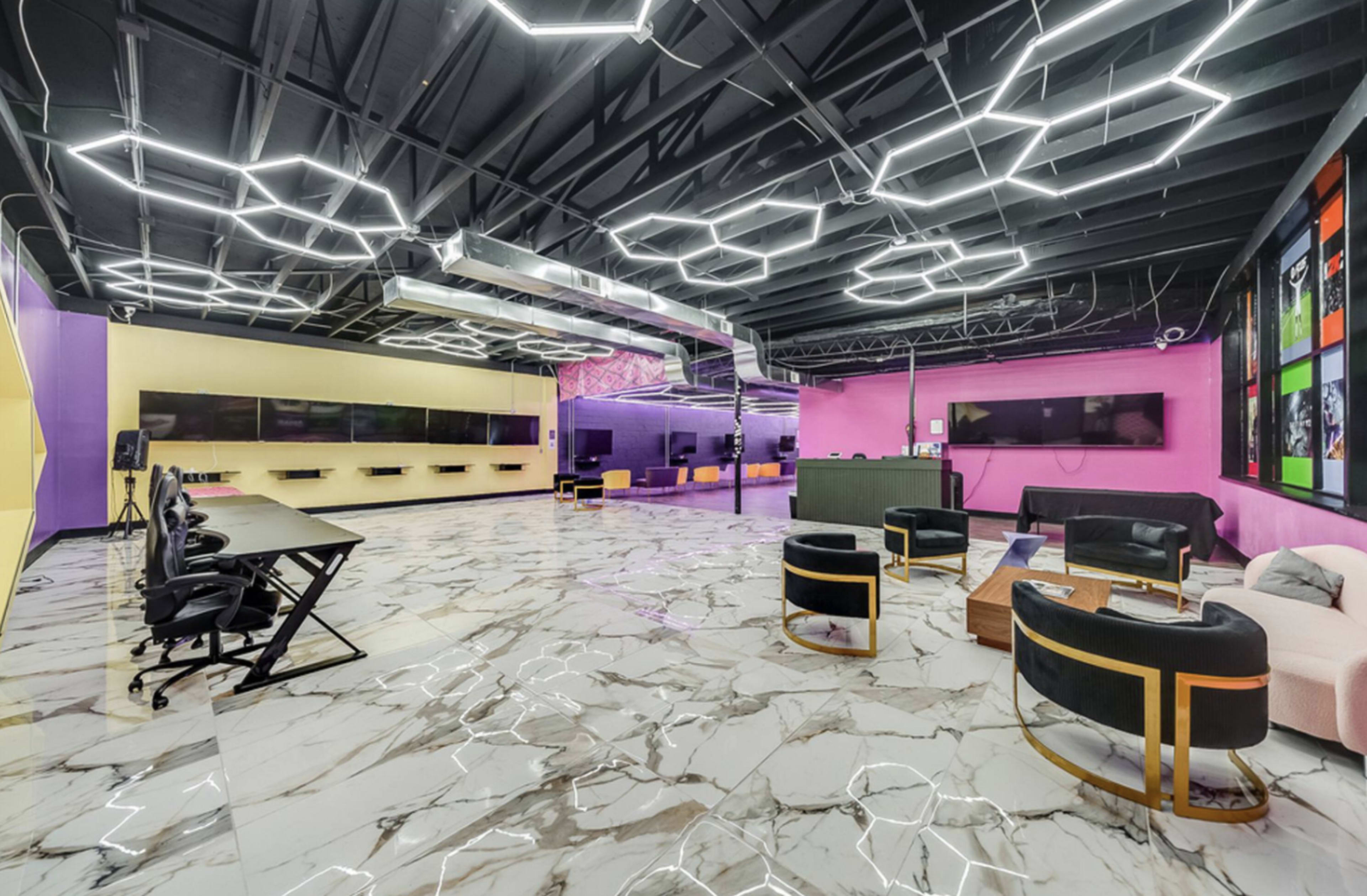 The image shows a modern, brightly colored gaming or multimedia room with marble flooring, neon lighting, and multiple screens mounted on the walls.