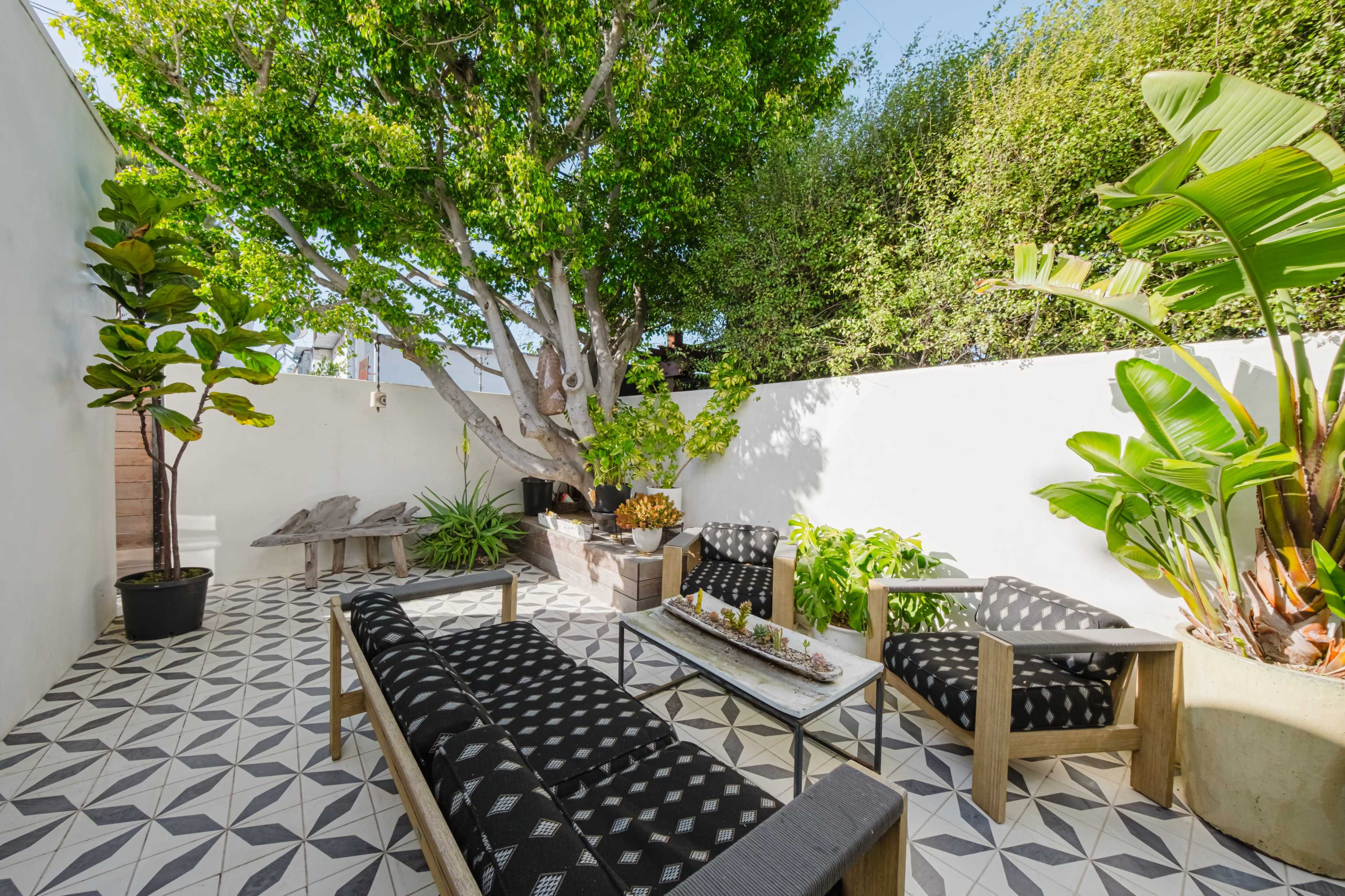 A small outdoor patio features patterned tiles, wooden furniture, and greenery, enclosed by white walls.
