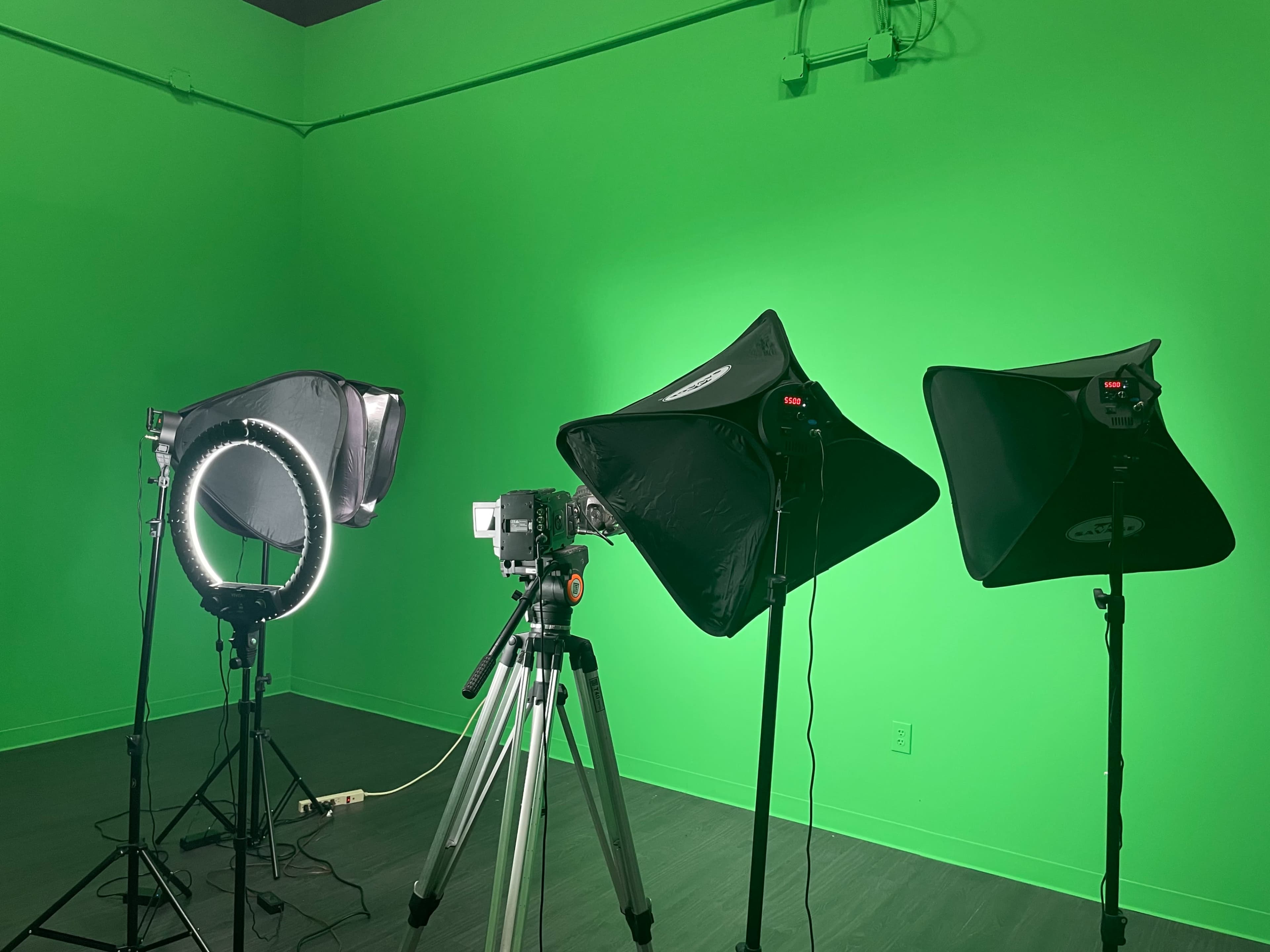 A green screen studio setup with three lighting fixtures and a camera on a tripod.