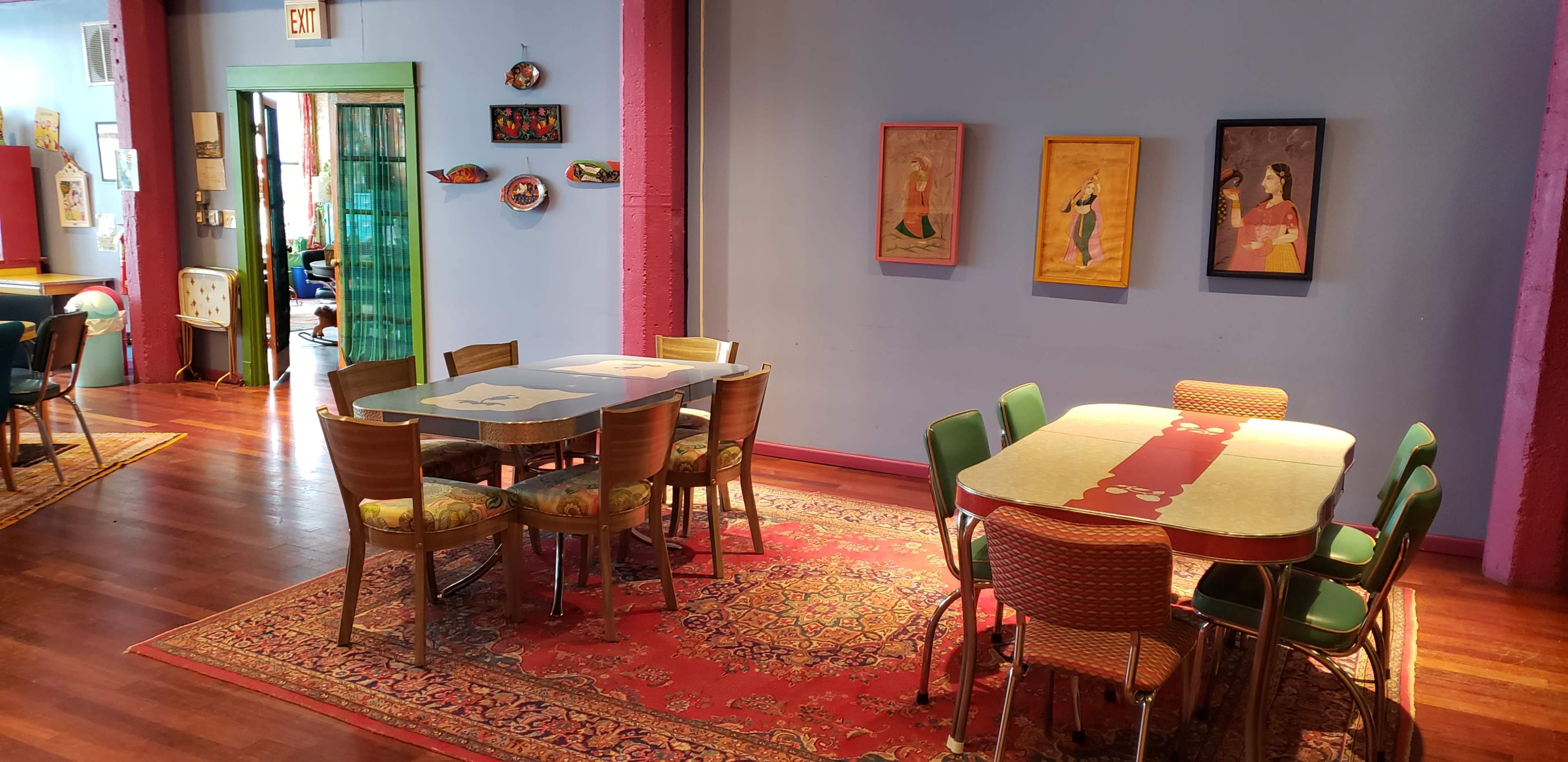 A colorful dining area with multiple tables, chairs, and framed artwork on the walls.