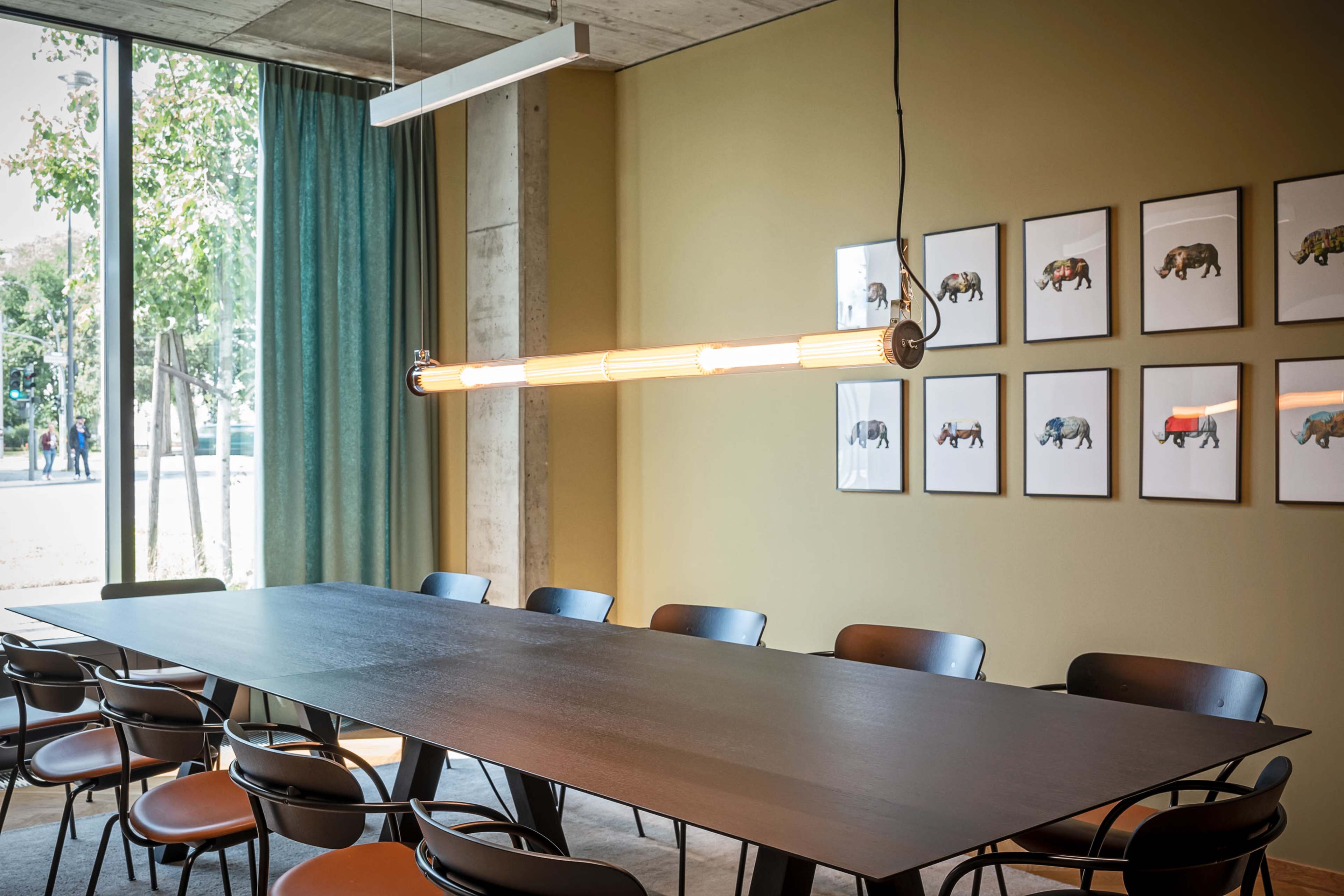 A modern conference room features a long black table, black chairs, and a series of framed animal illustrations on the wall, with natural light coming in through large windows.