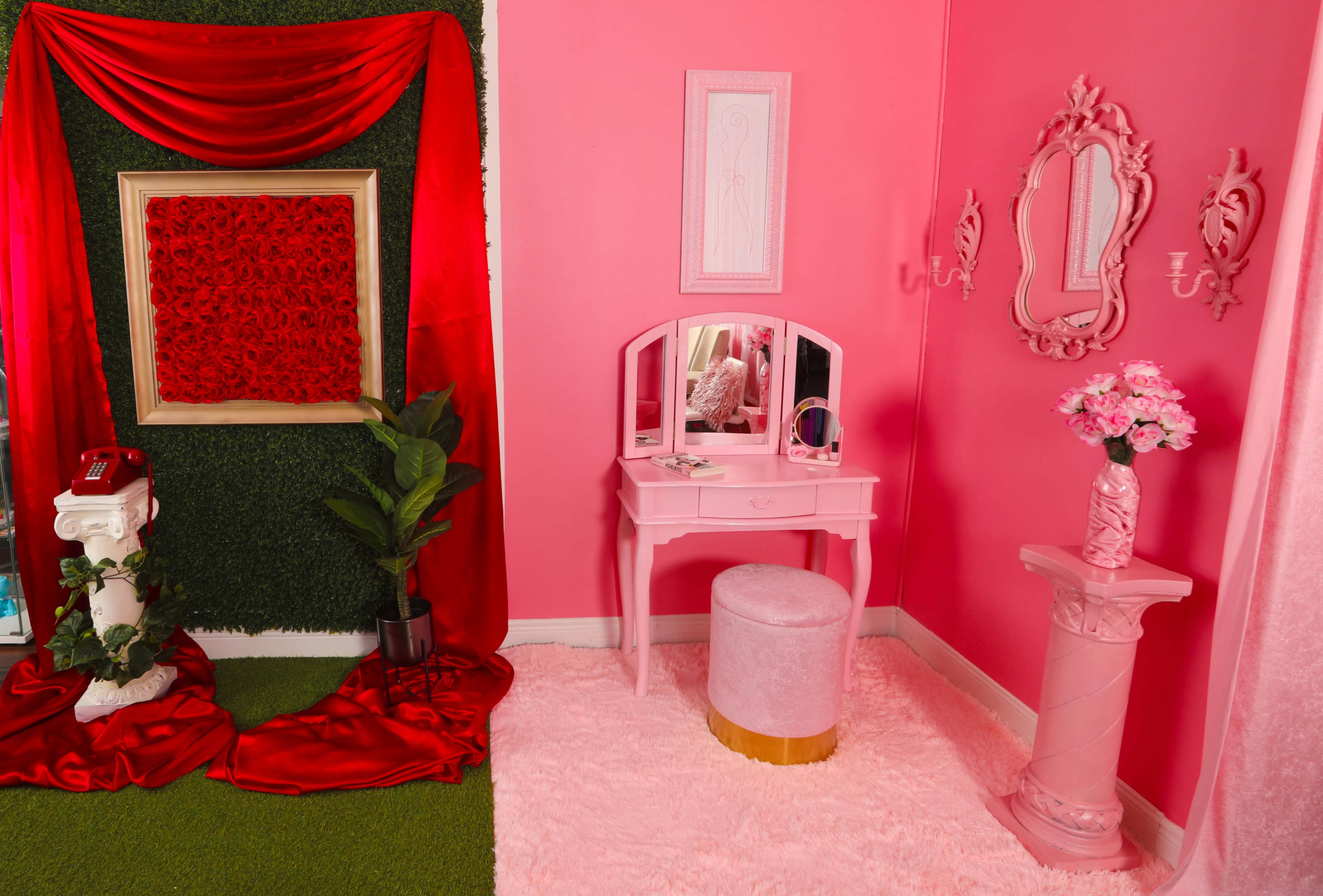 The scene features a pink-themed interior with a vanity set, decorative mirrors, a floral arrangement, and vibrant red drapery against a pink wall.