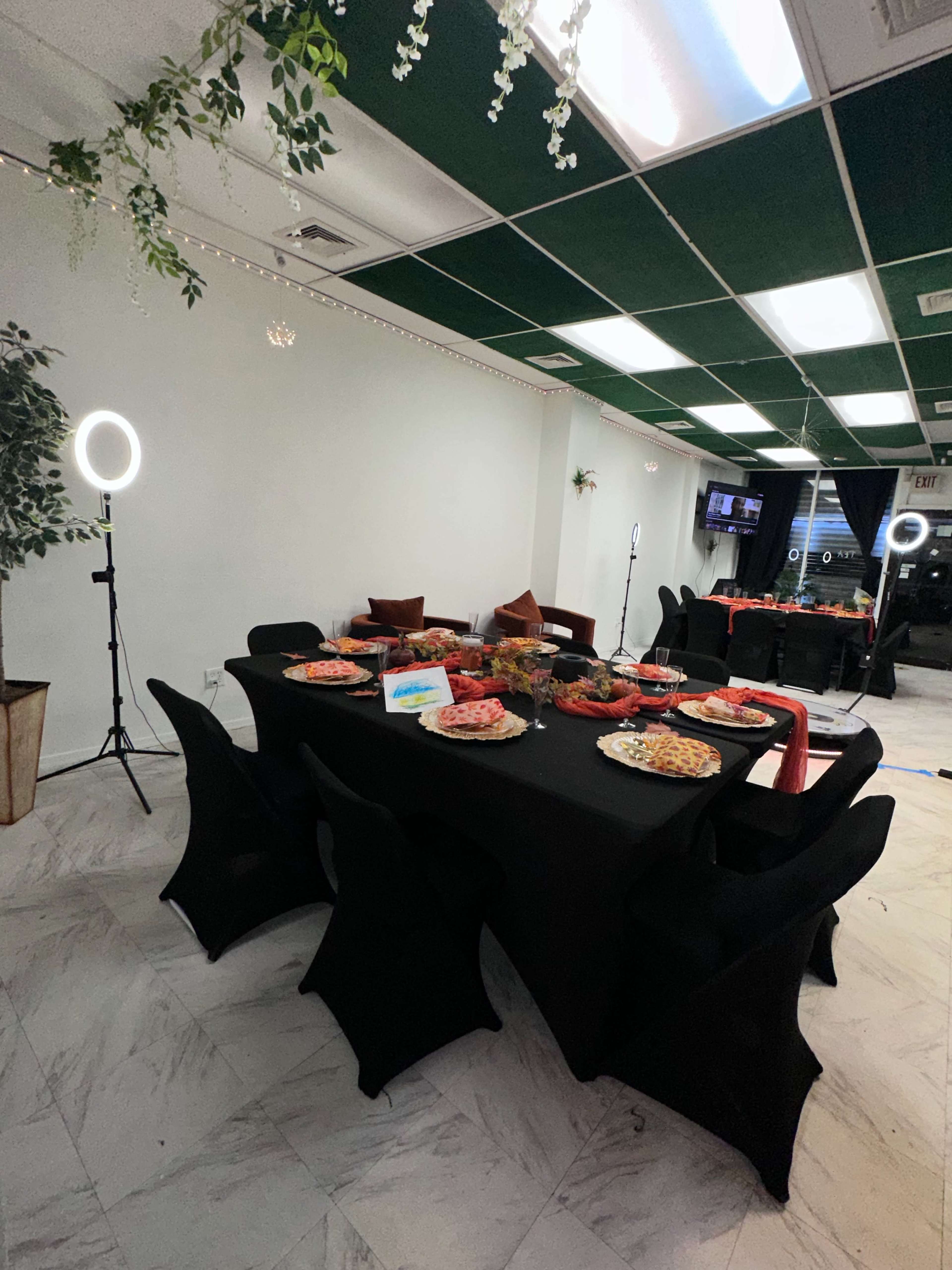 A decorated dining area features a black table set with various dishes and snacks, surrounded by chairs with black covers.