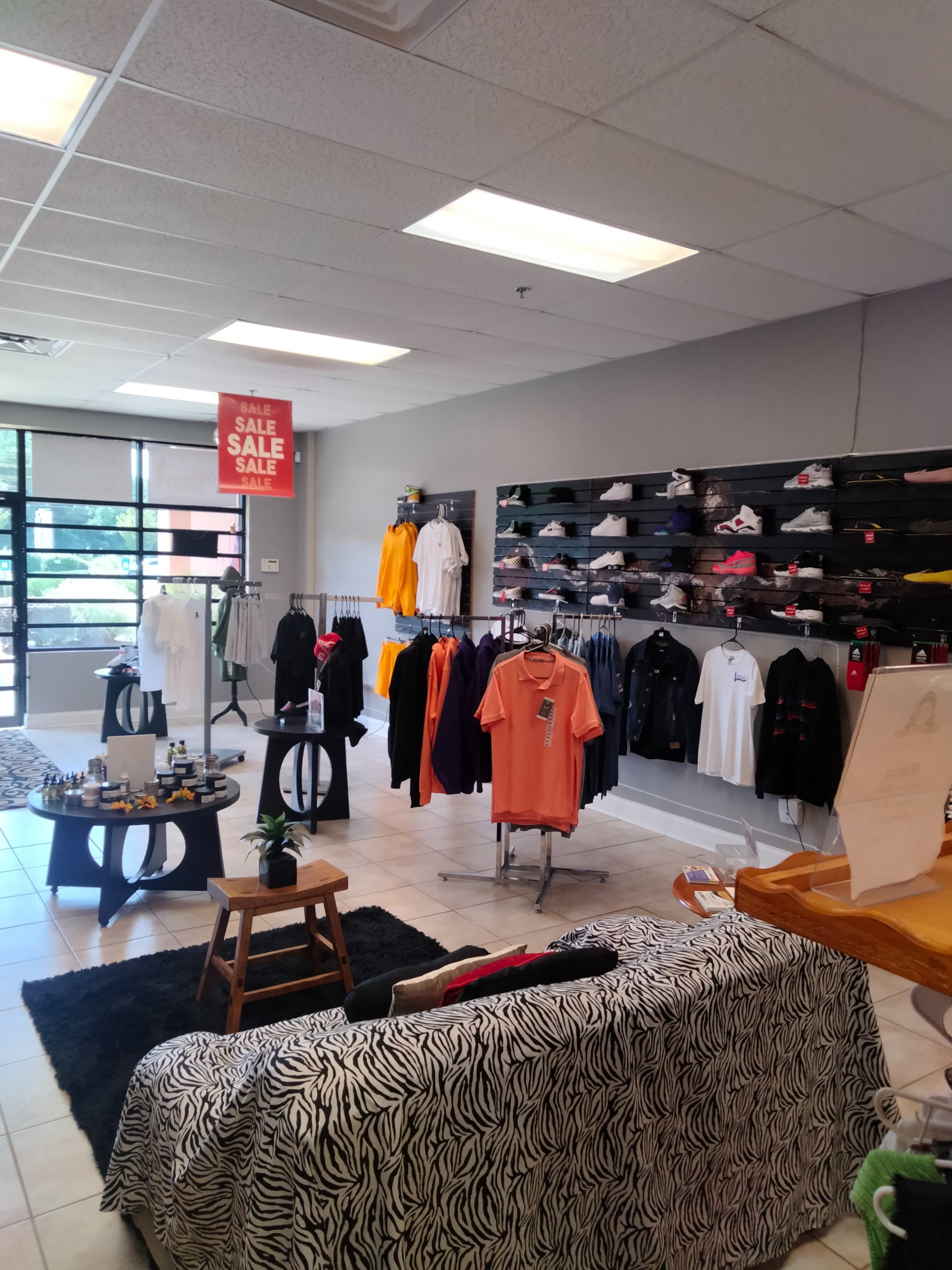 A clothing store interior with racks of apparel, a seating area, and promotional sale signage.