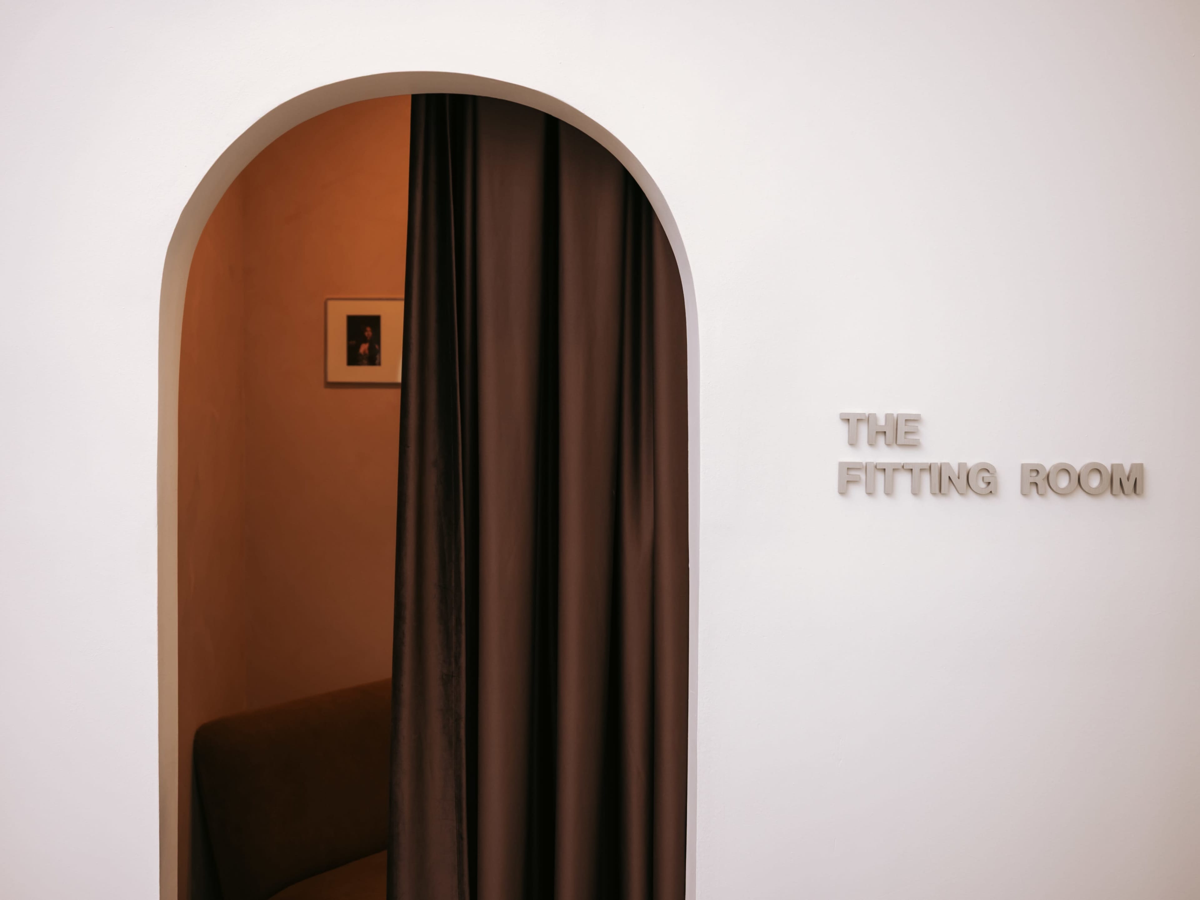 A fitting room entrance features an arched opening with a curtain and a sign that reads "THE FITTING ROOM."