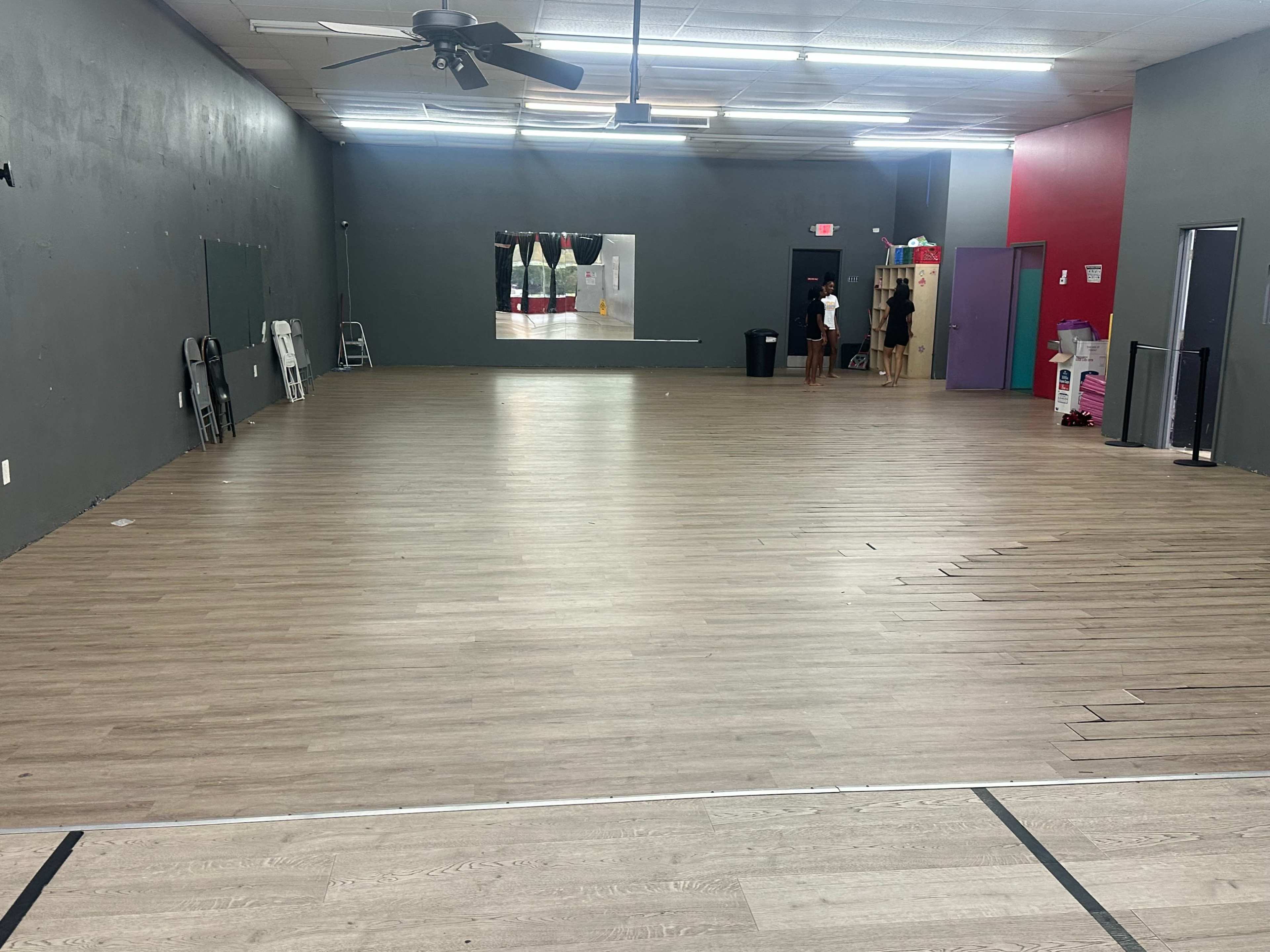 The image shows a spacious interior with a wooden floor, partially empty walls, and some furniture along the side.