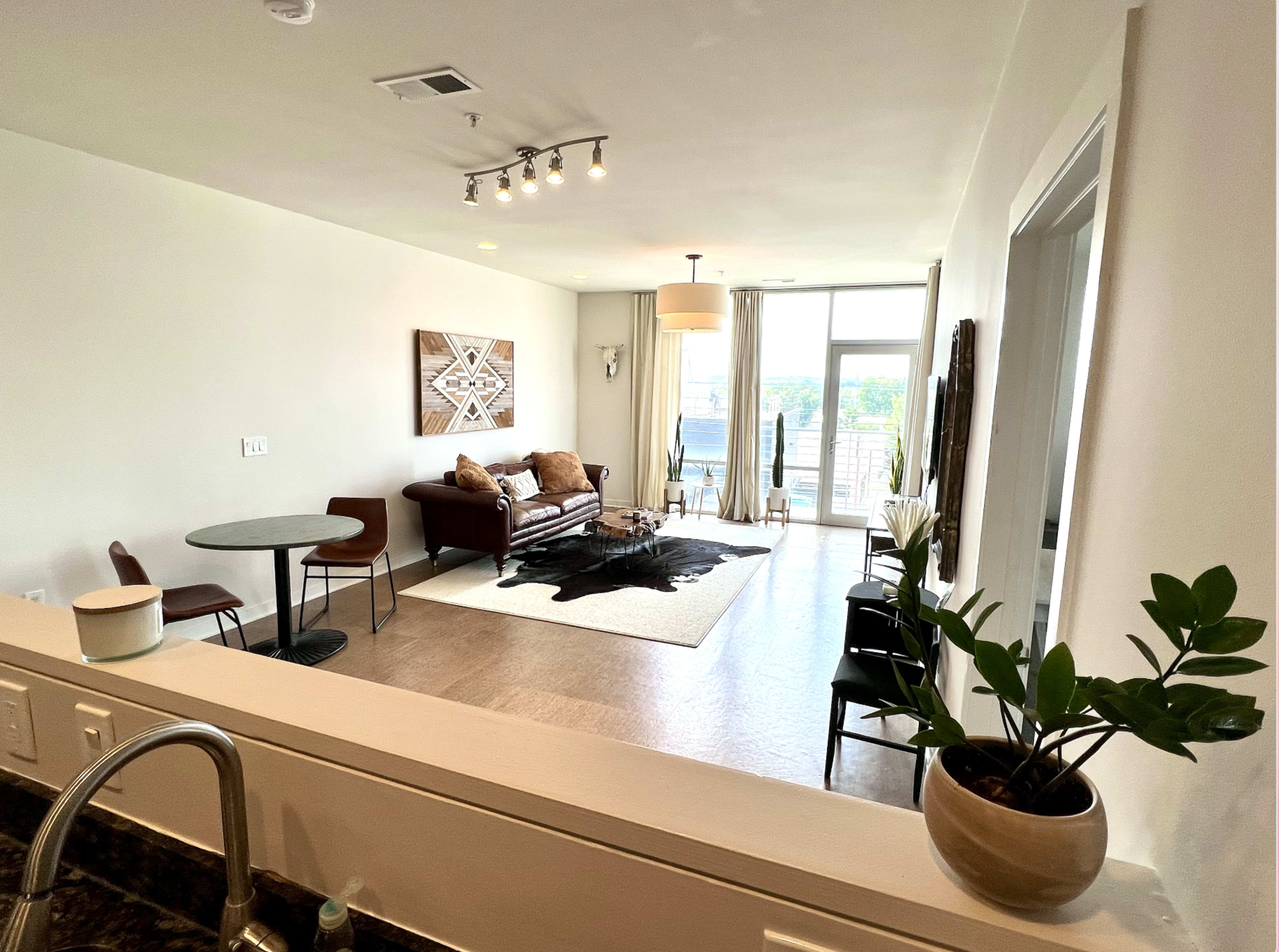 A modern living room with a sofa, a small dining table, and large windows showcasing a view.